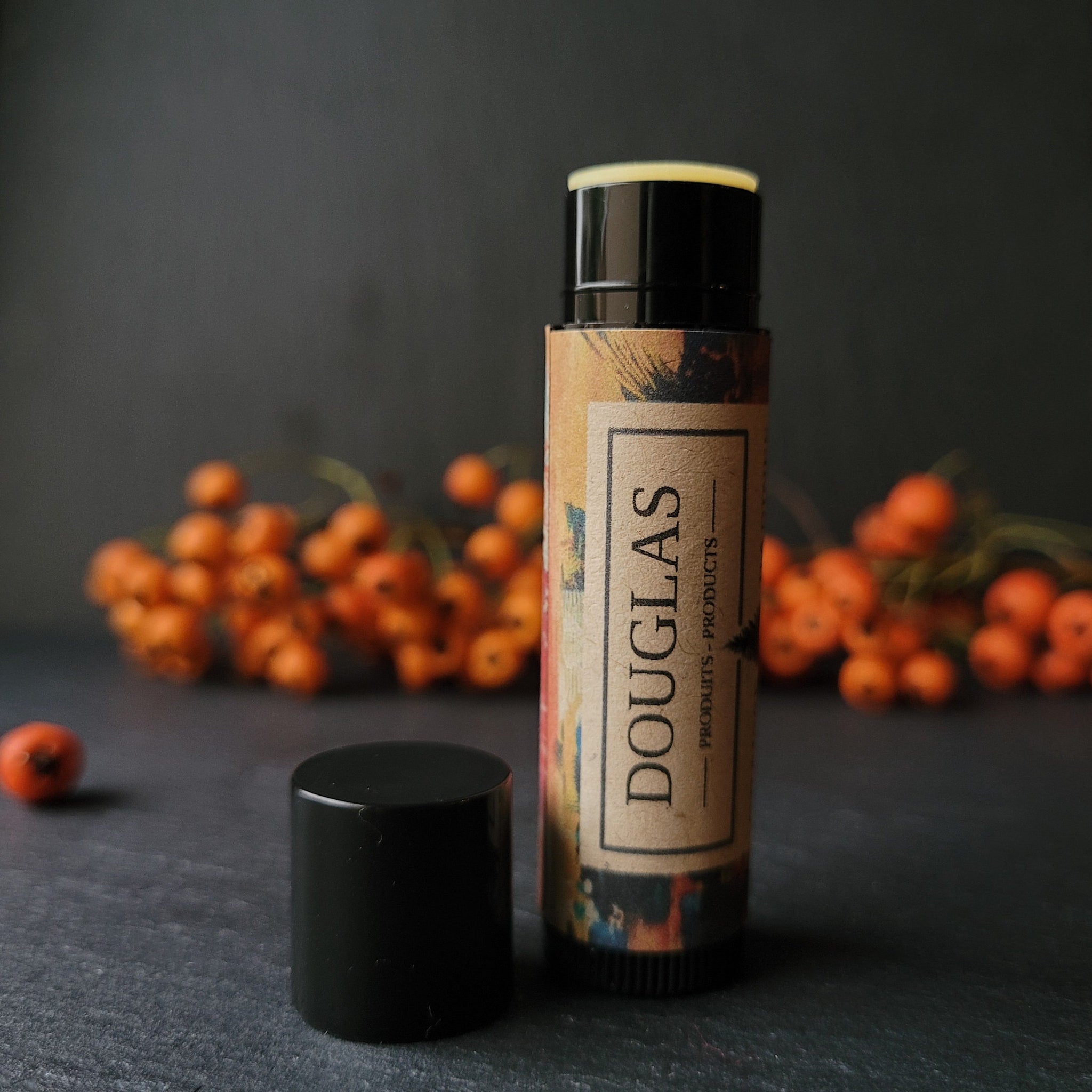 Lip balm with black cap, tan label with DOUGLAS text, and colorful pattern on the label