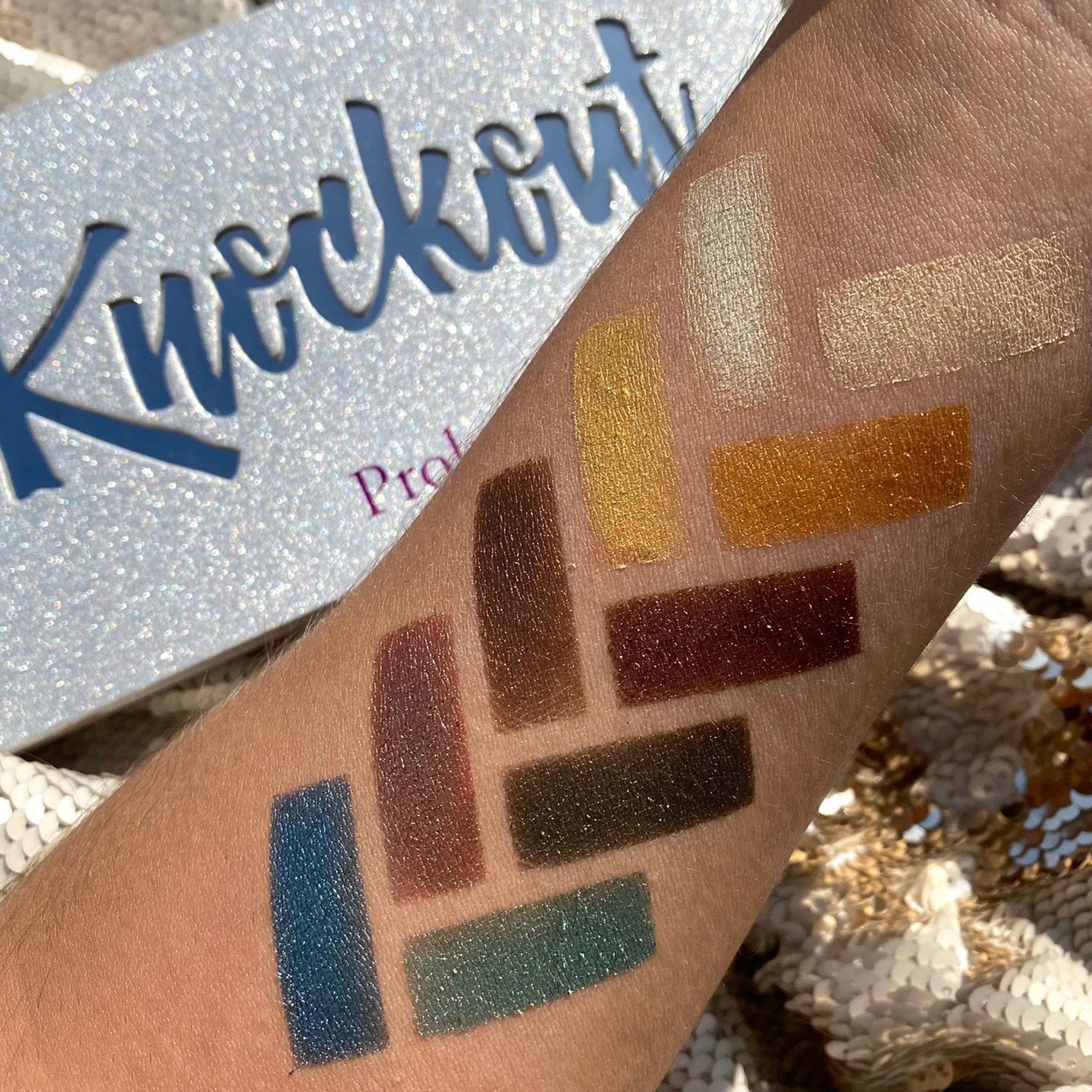 Eyeshadow swatches in various metallic colors on skin, with "Knockout" palette visible