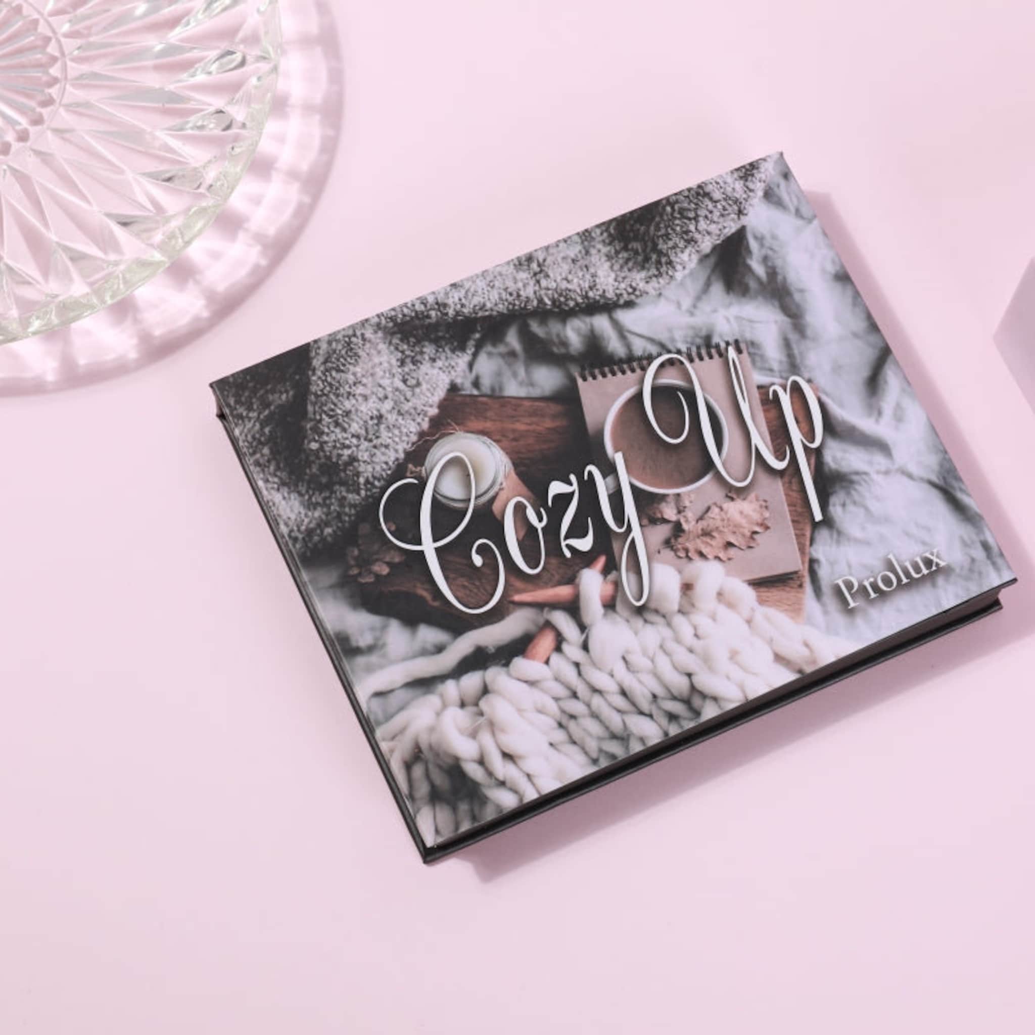 Cozy Up book with black cover, white script text, and Prolux brand name on pink background