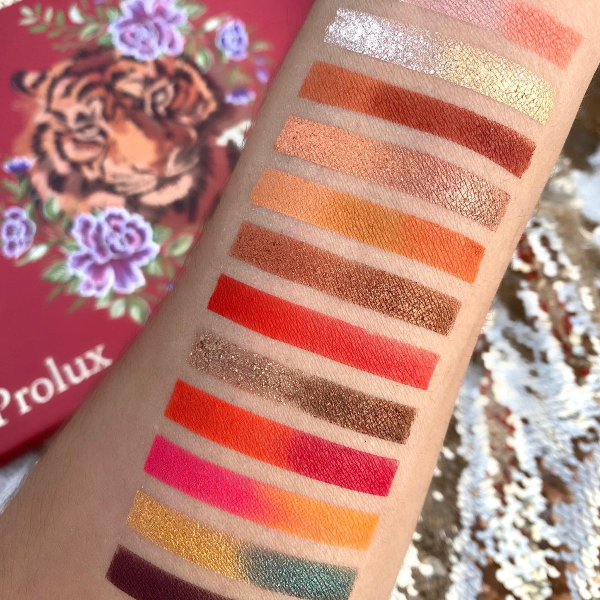 Eyeshadow swatches in multiple colors, including orange, pink, and gold, applied to arm