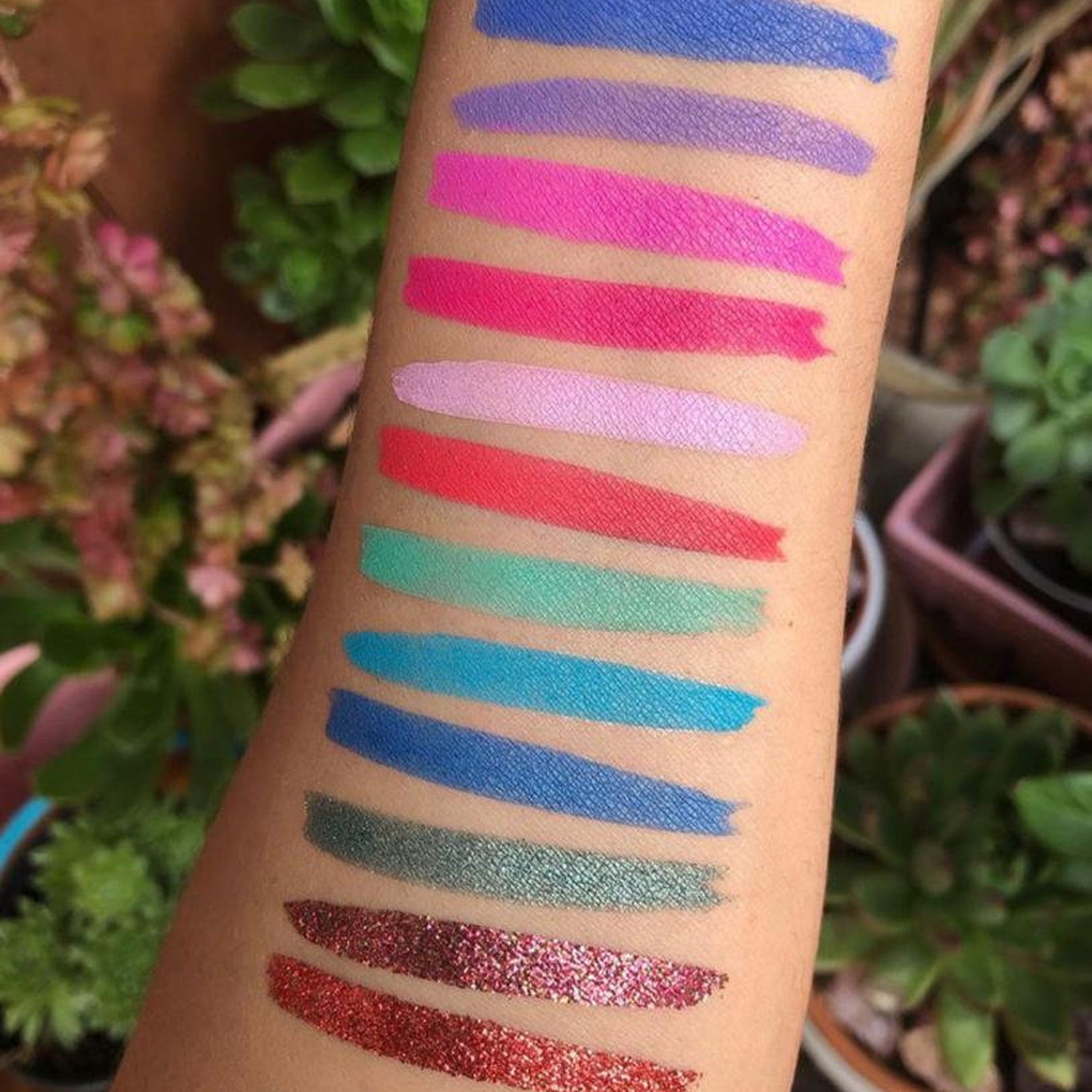 Lipstick swatches in various colors including pink, red, blue, and glitter, shown on arm for color comparison
