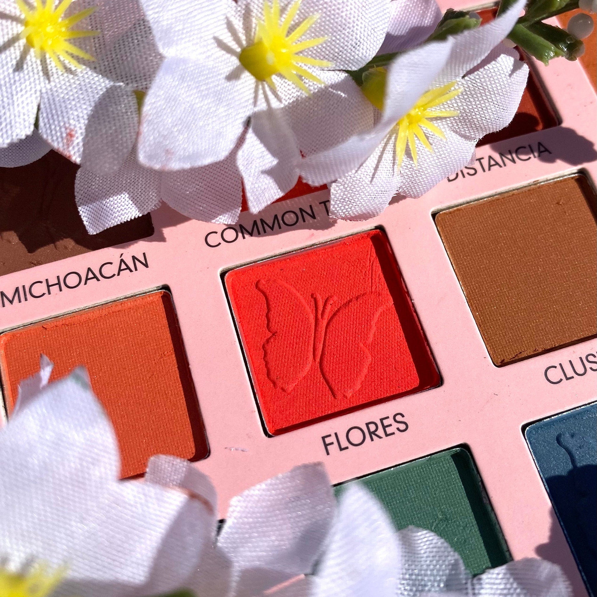 Eyeshadow palette with red, orange, and brown shades, floral accents, and butterfly detail on red shadow