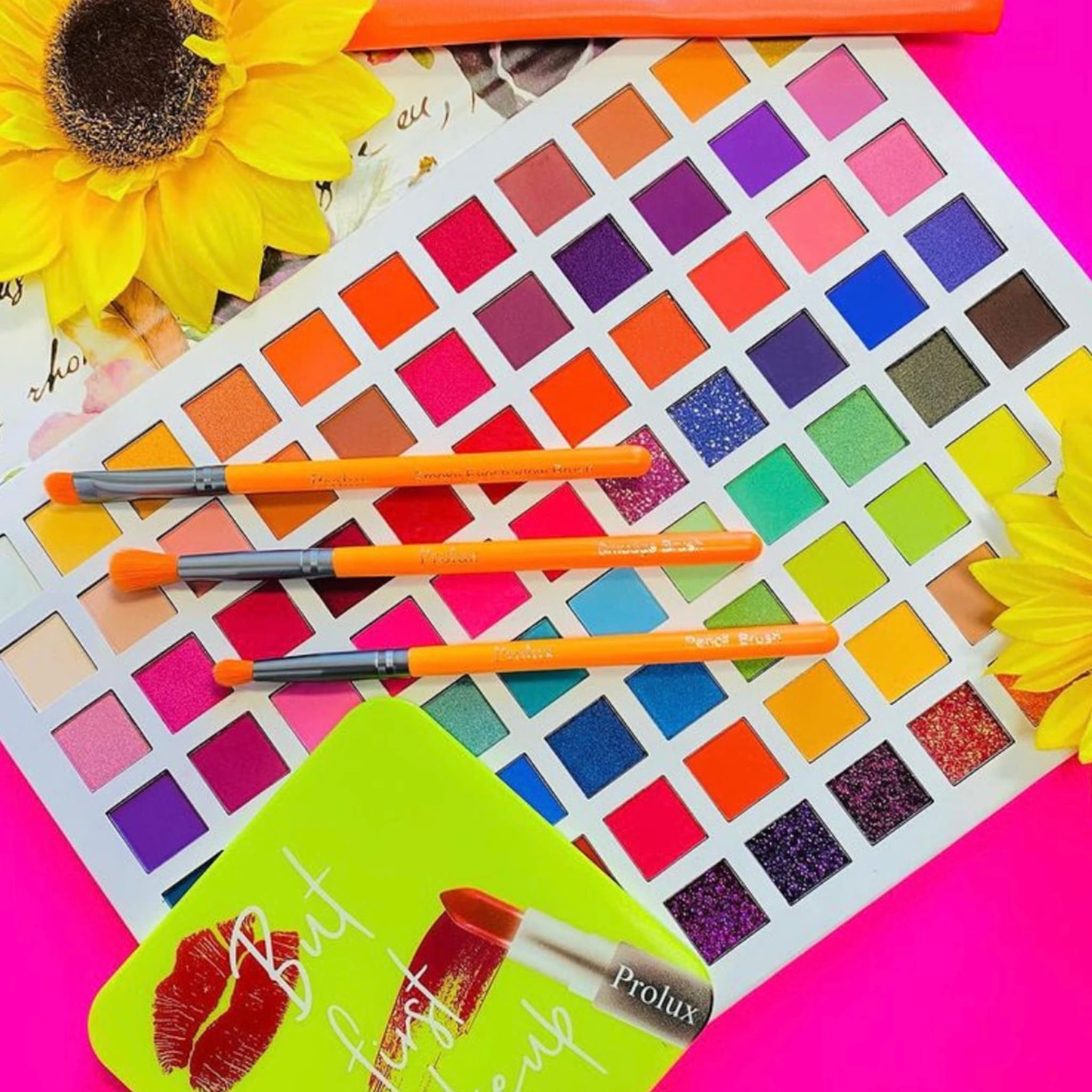 Eyeshadow palette with multiple colors, orange brushes, and Prolux branding on a pink background