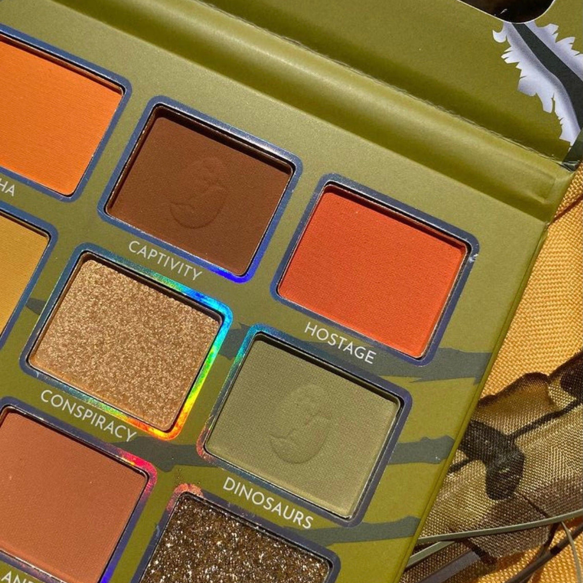 Eyeshadow palette with olive green and brown shades, metallic silver trim, and camouflage pattern on the packaging