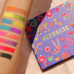 Eyeshadow palette with colorful swatches, glitter, and "ALEBRIJE" text on purple box