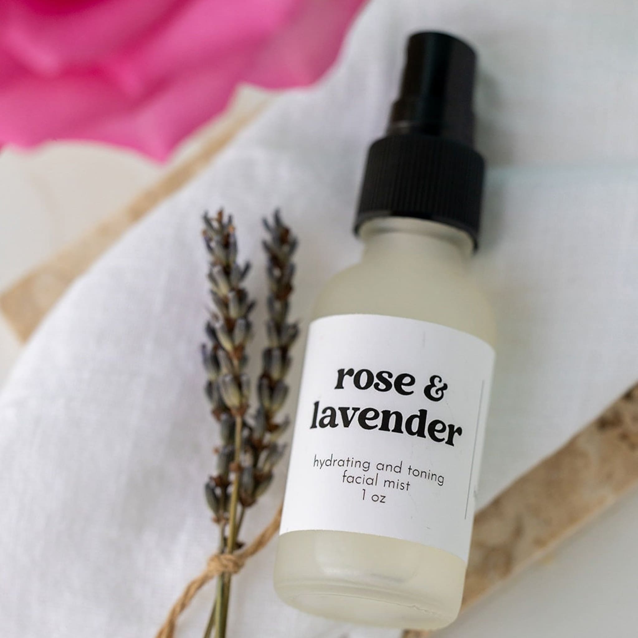 Facial mist bottle with black cap, white label, and lavender sprigs on white cloth