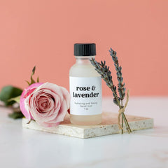 Facial mist bottle with black cap, white label, and rose & lavender text, on stone block