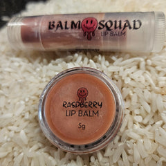 Lip balm with raspberry flavor in clear container, Balm Squad branding, and a pinkish hue