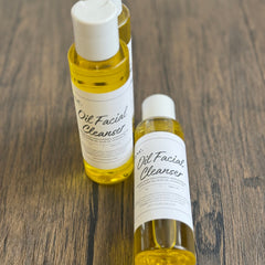 Oil facial cleanser bottles, yellow liquid, white labels, on wood surface