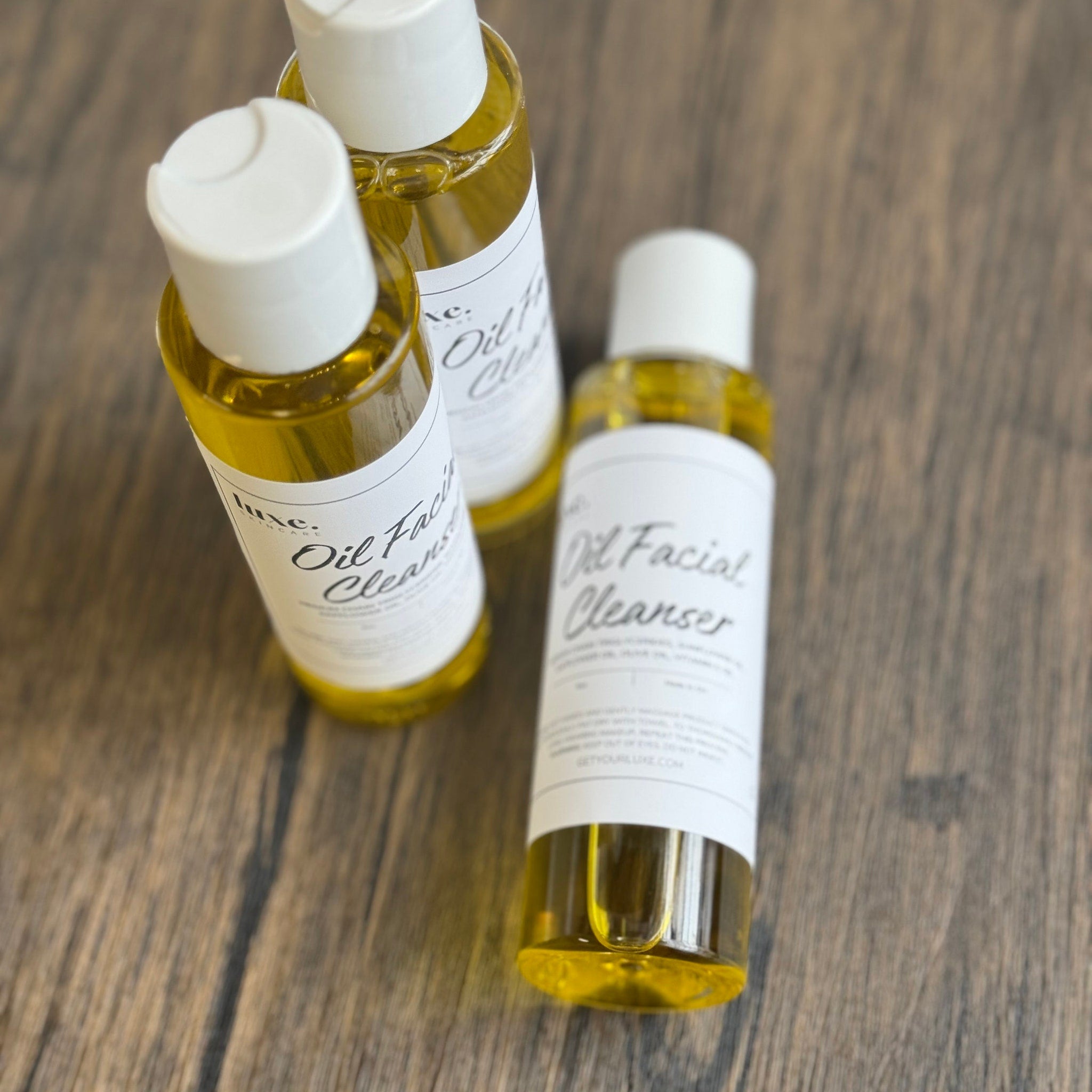 Oil facial cleanser bottles with yellow liquid, white labels, and white caps on wood surface