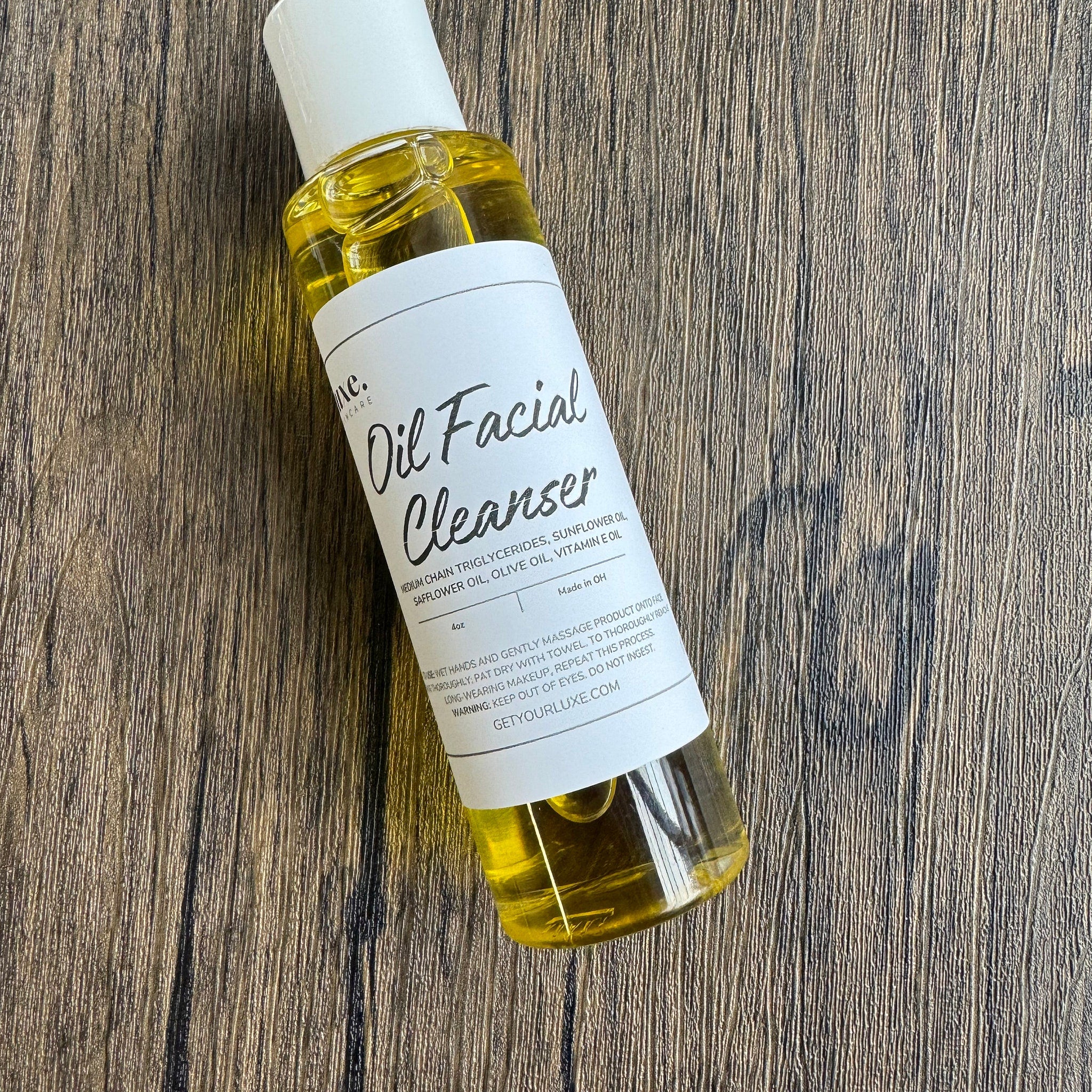 Oil facial cleanser bottle with yellow liquid, white label, and wooden background