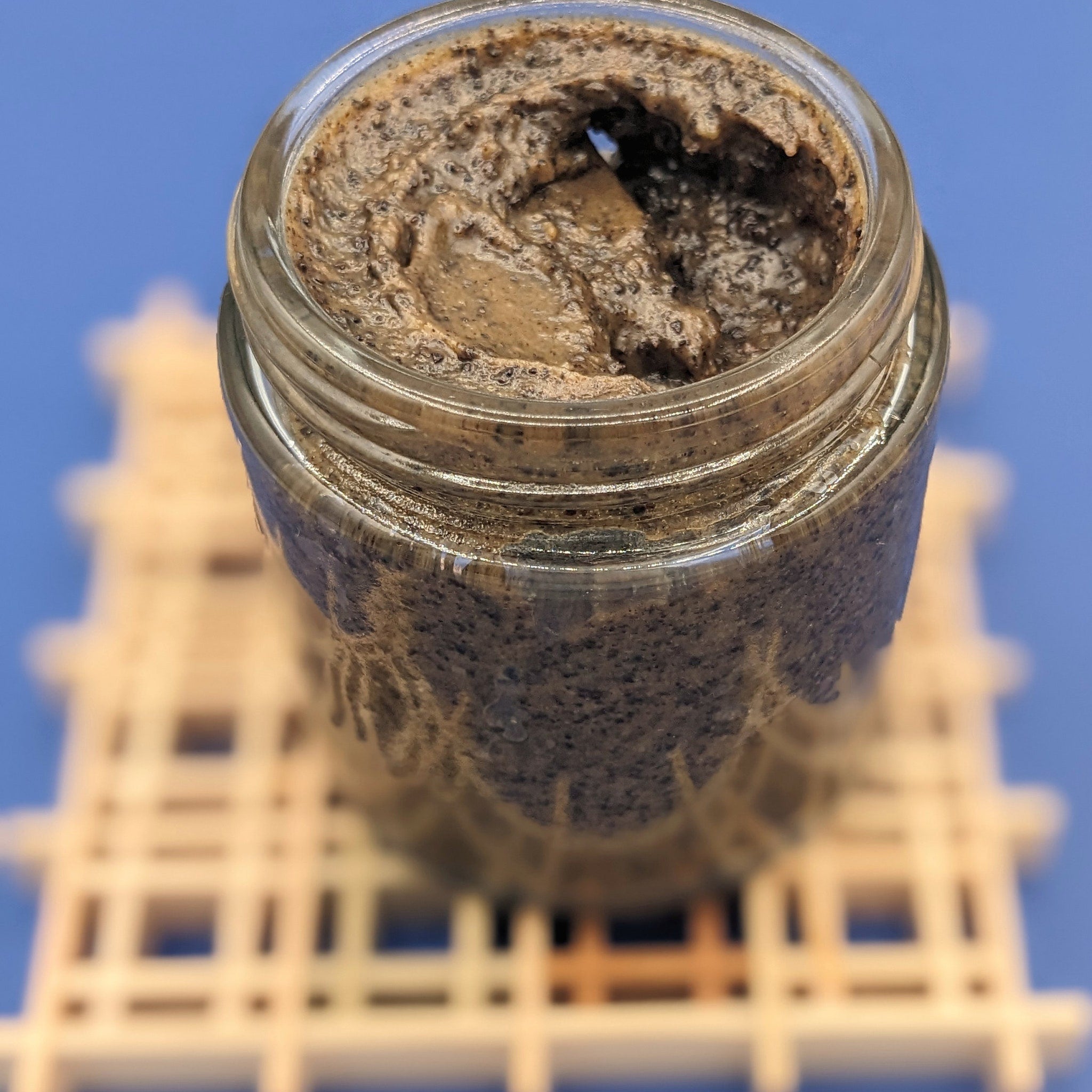 Brown paste in a glass jar, textured surface, visible seeds, on a white structure with a blue background
