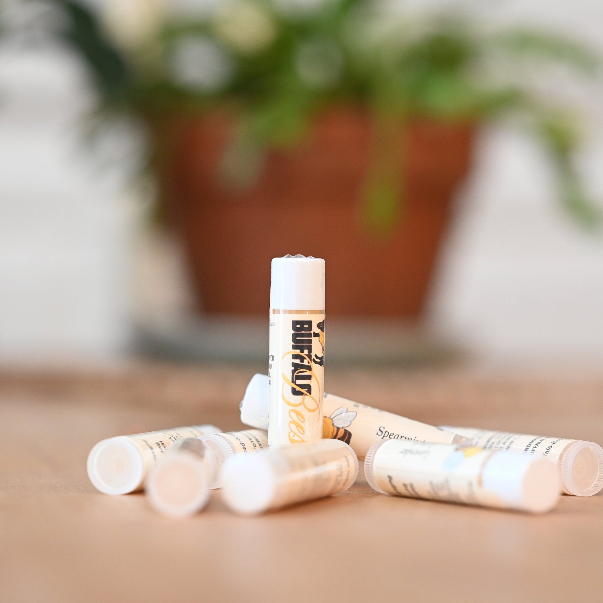 Lip balm tubes with white caps, tan labels, and Buffalo Bees branding, scattered on a surface