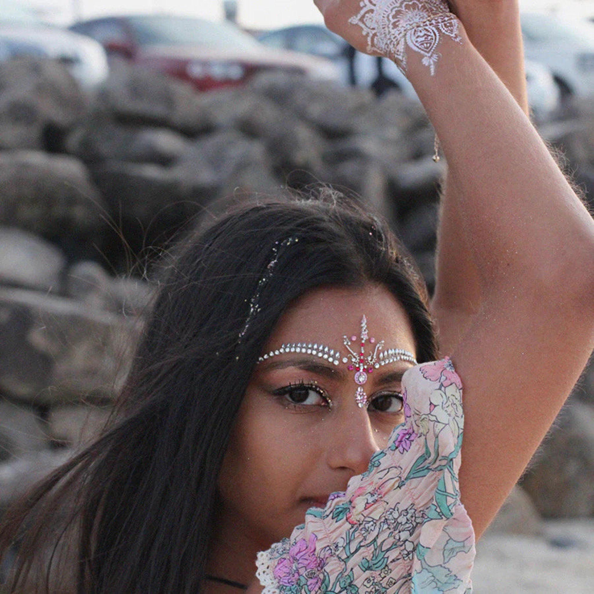 White henna arm art with floral patterned fabric and face jewels on woman's face