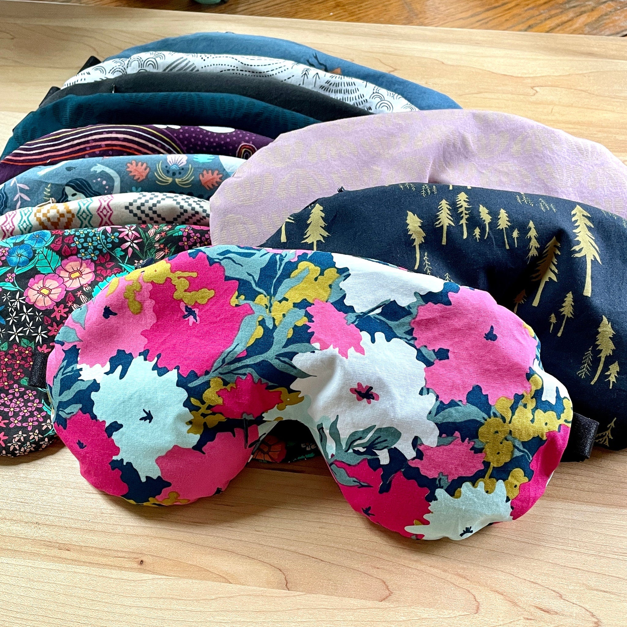 Eye masks with floral pattern, pink and blue fabric, and various designs displayed on wood surface