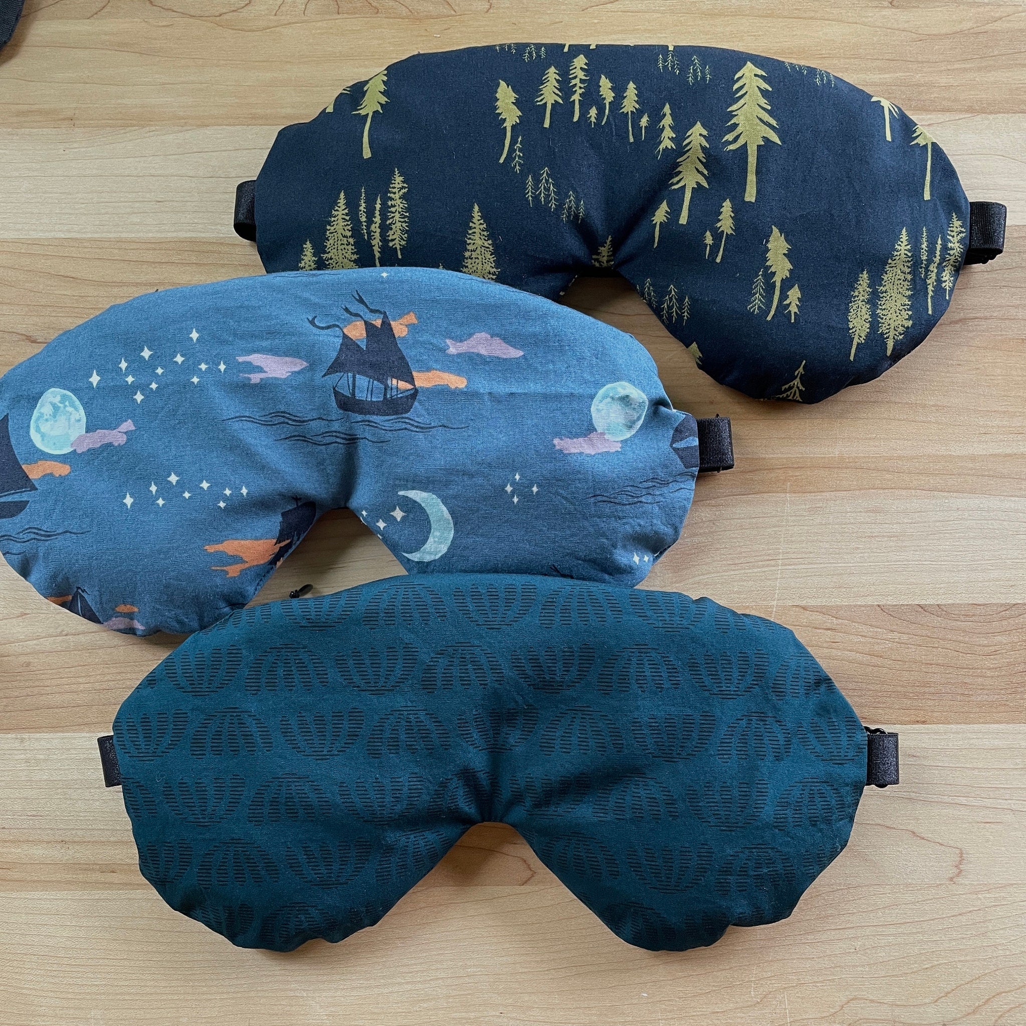 Sleep masks with various patterns, including navy with gold trees, blue with moon, and teal geometric pattern