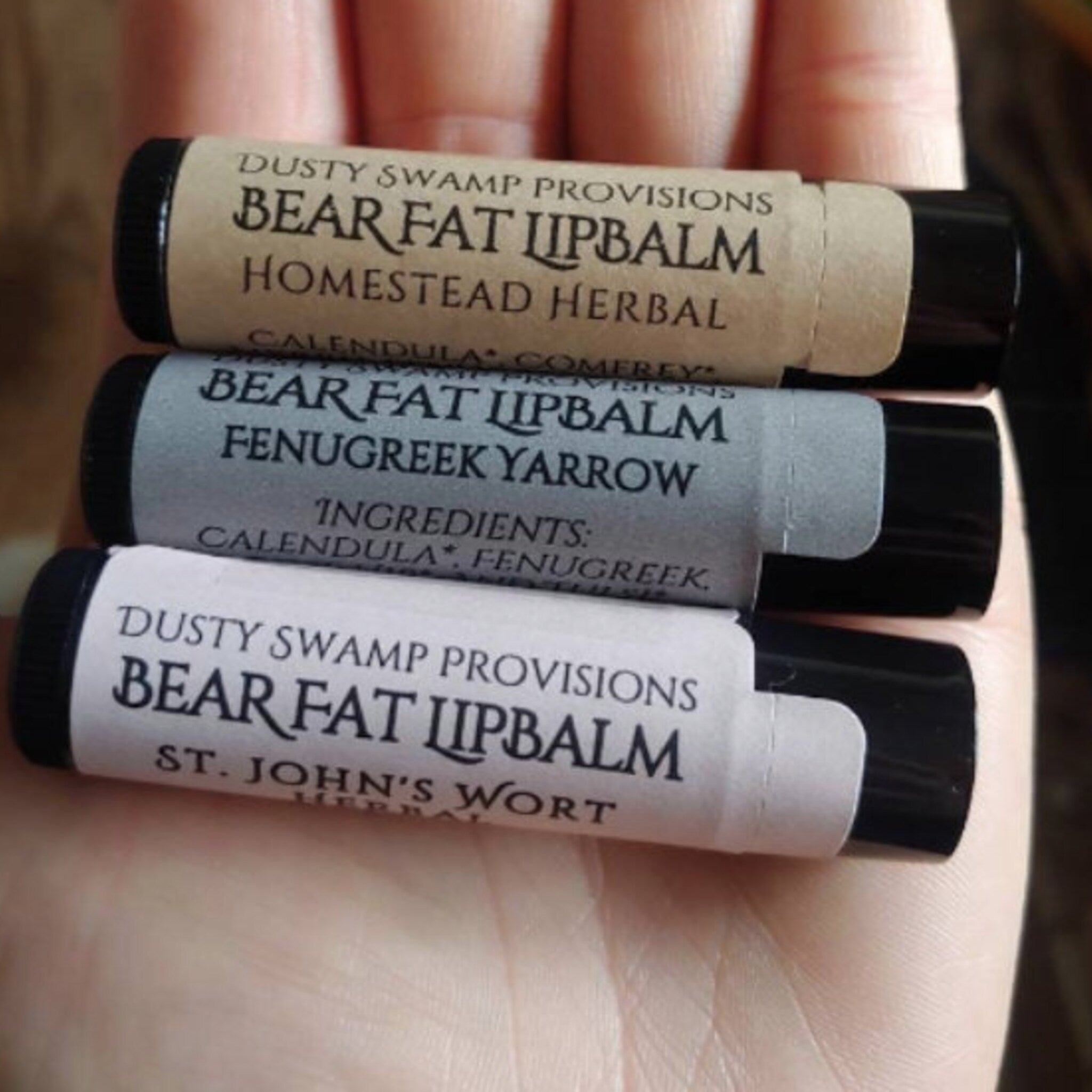 Lip balm tubes with Homestead Herbal labels in brown, gray, and white, held in hand