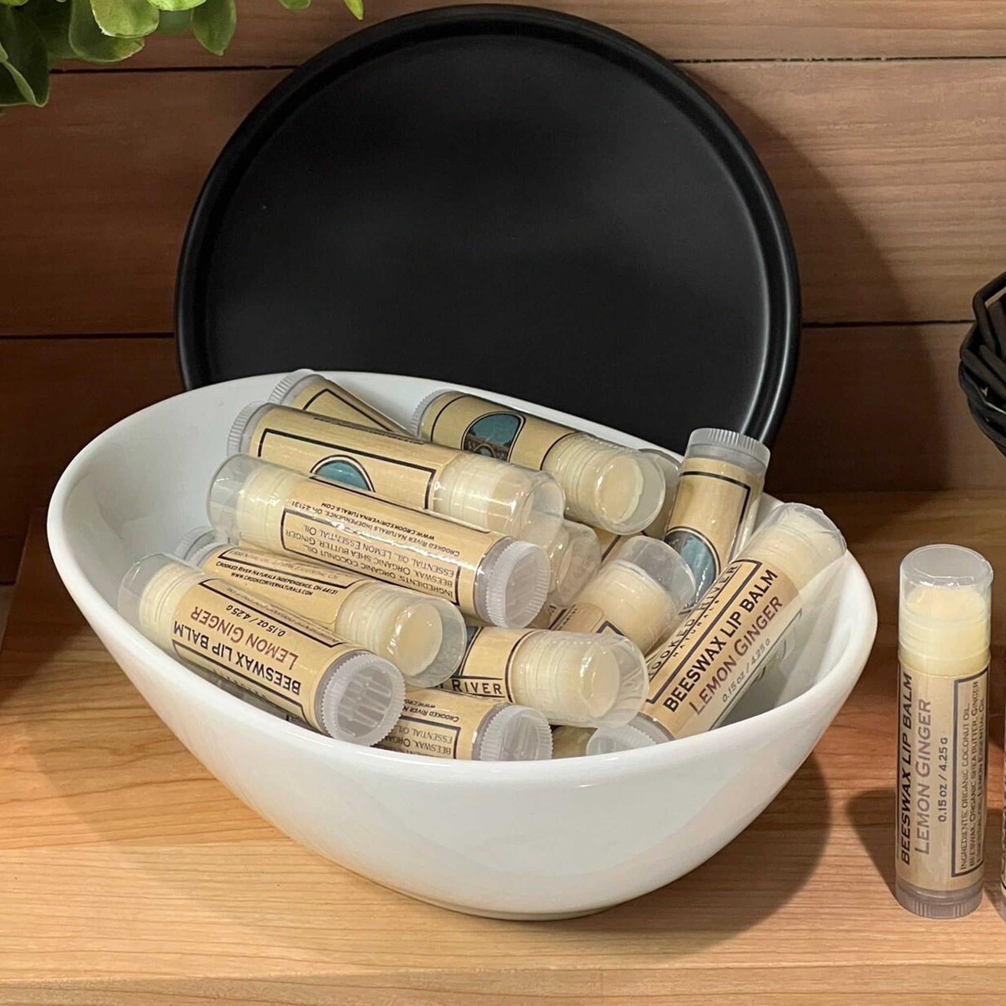 Lip balm tubes in clear plastic with tan labels, in white bowl, "Beeswax Lip Balm" text visible