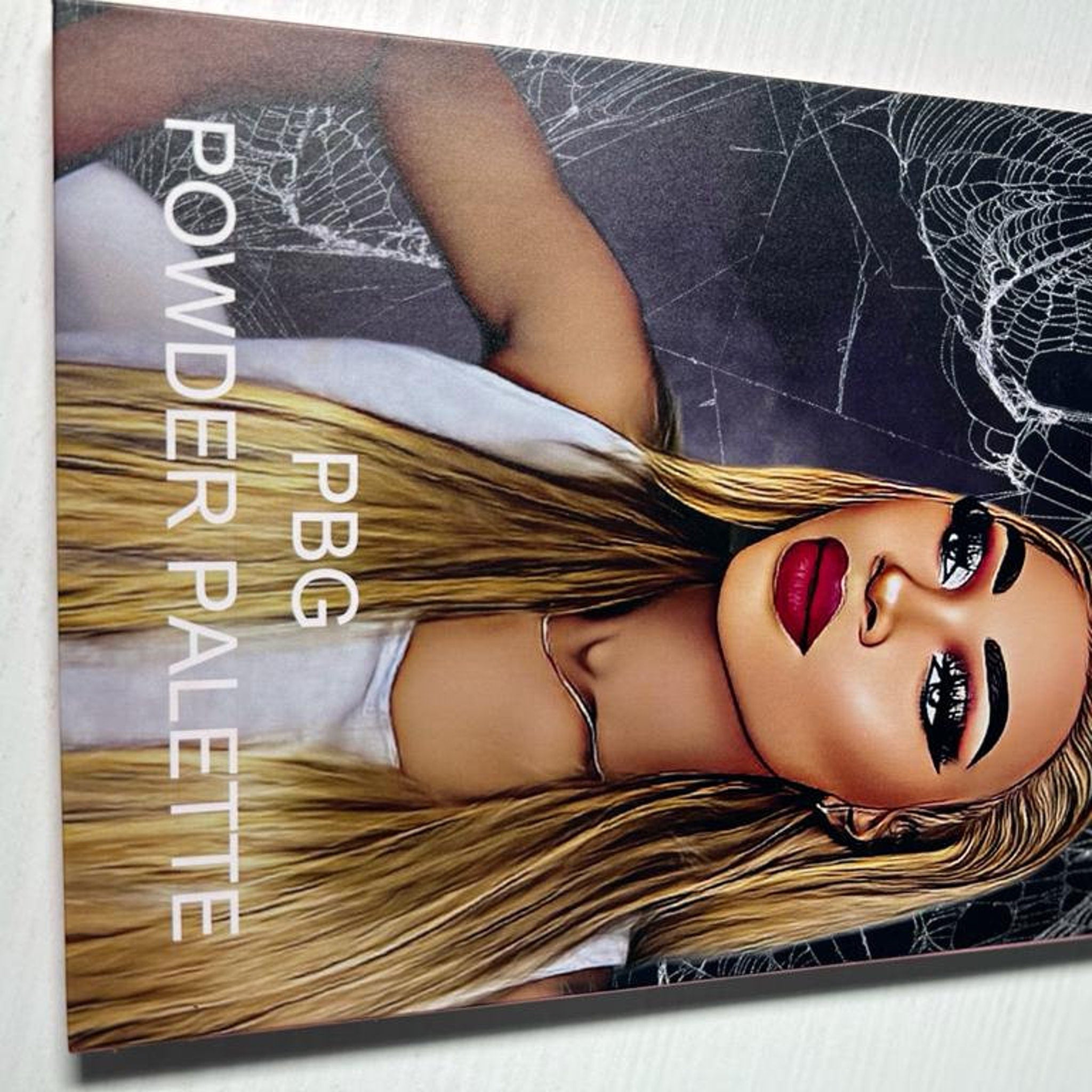 Powder palette with blonde hair, red lips, and spiderweb background design