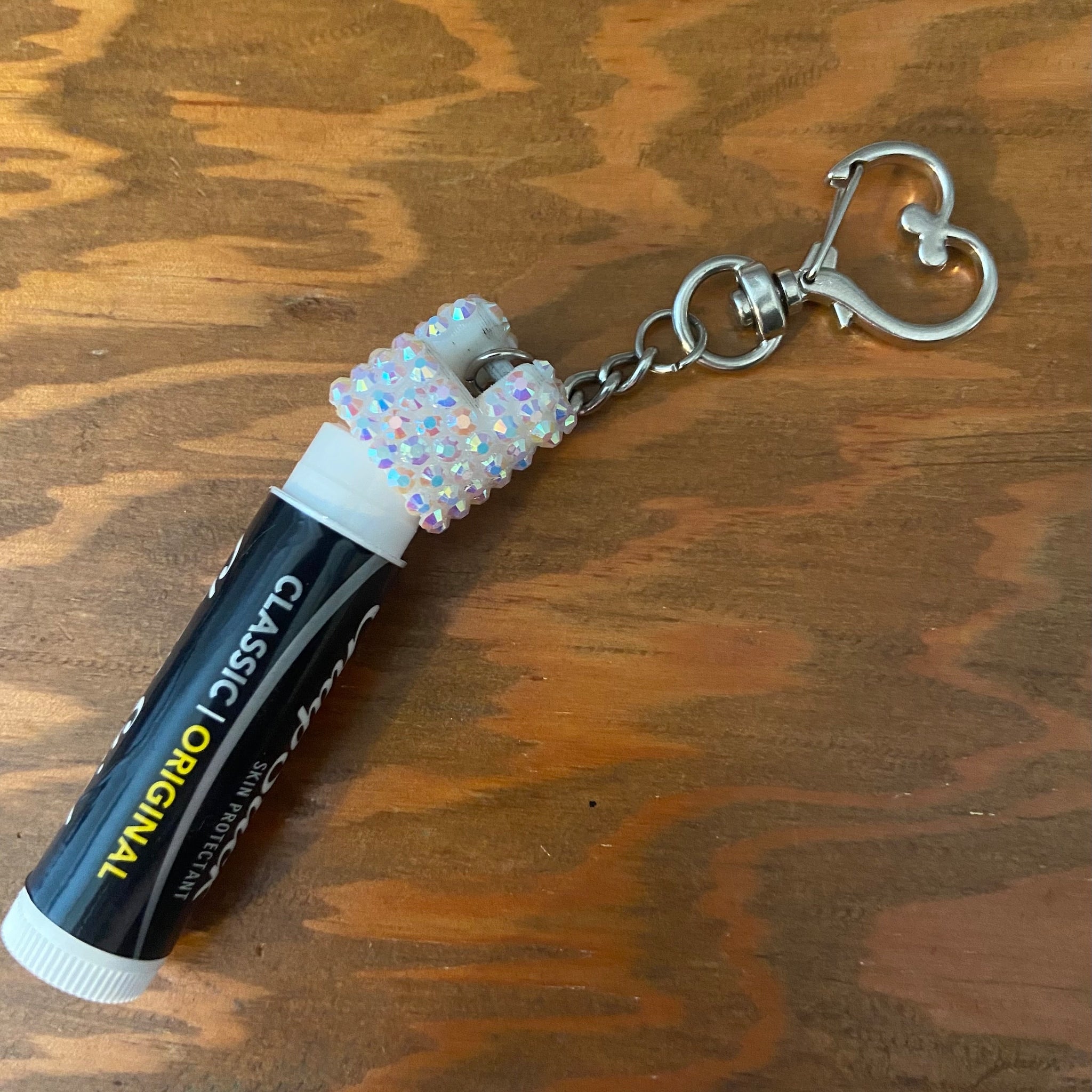 Lip balm tube with heart-shaped charm, black and white tube, silver chain and clasp, iridescent heart charm