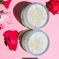 Body scrub with white and tan speckled contents in clear glass jars, with red flowers on pink background