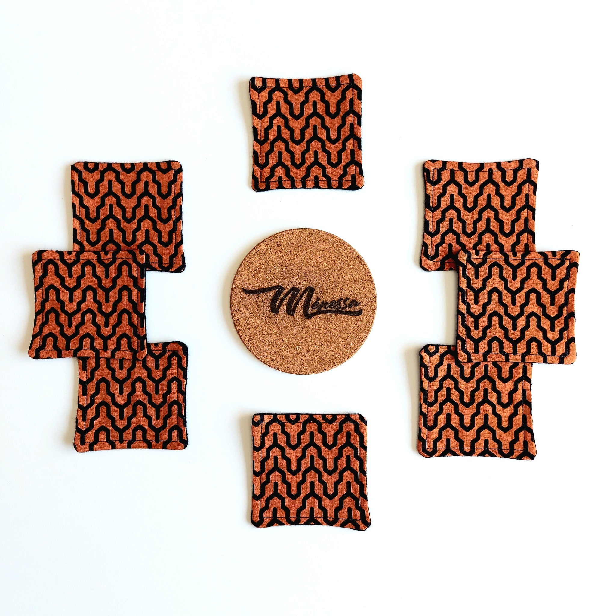 Coasters with orange and black geometric pattern, cork center with "Mènessa" text, on white surface