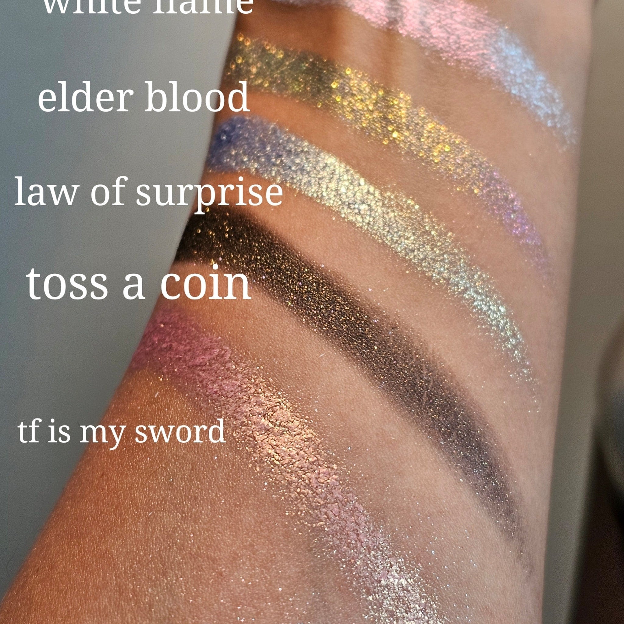 Side view of five multichrome pressed eyeshadows showing color shift from teal to purple in compact palette