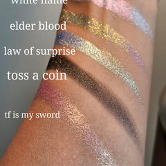 Side view of five multichrome pressed eyeshadows showing color shift from teal to purple in compact palette