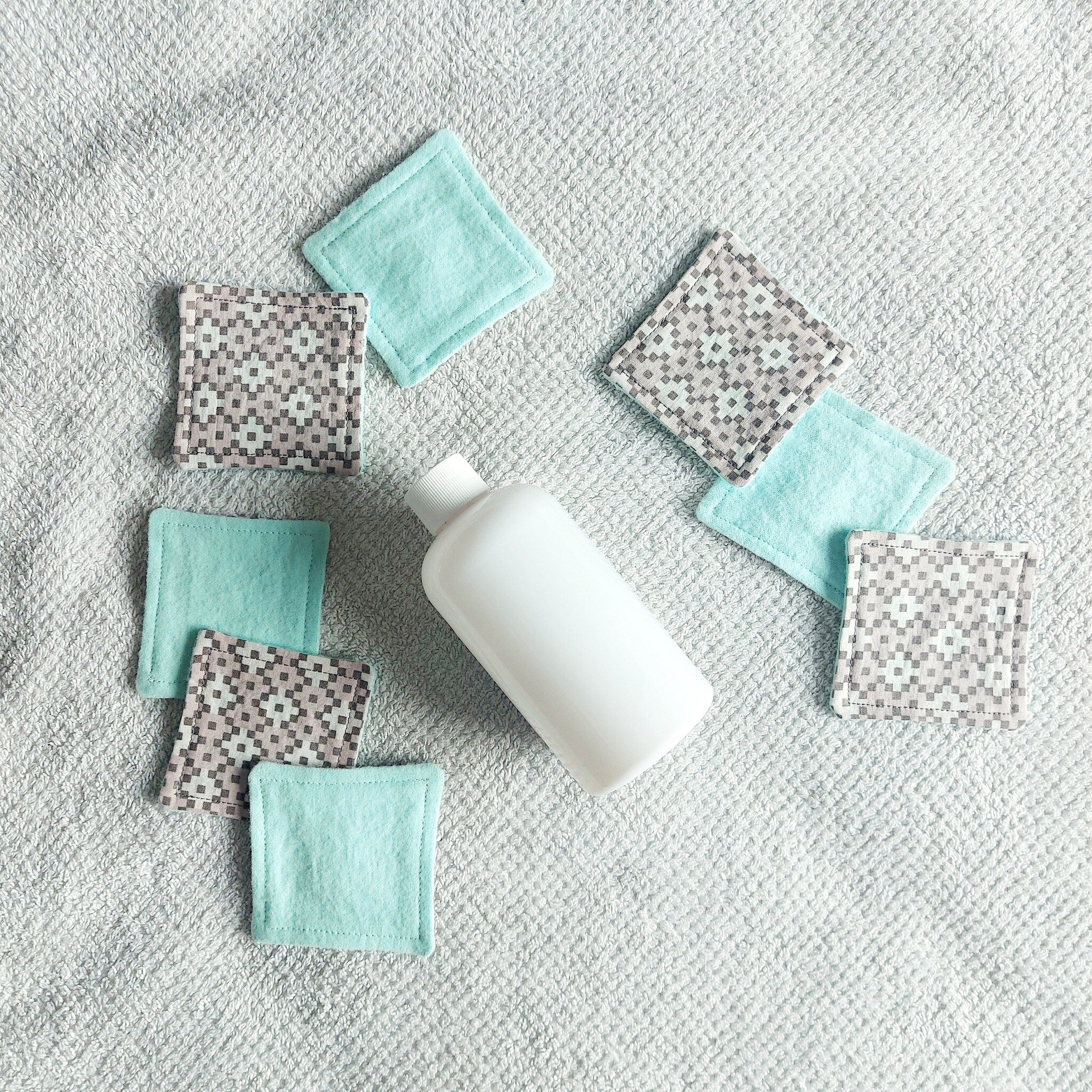 Makeup remover pads, fabric, square, patterned and teal, with bottle on towel