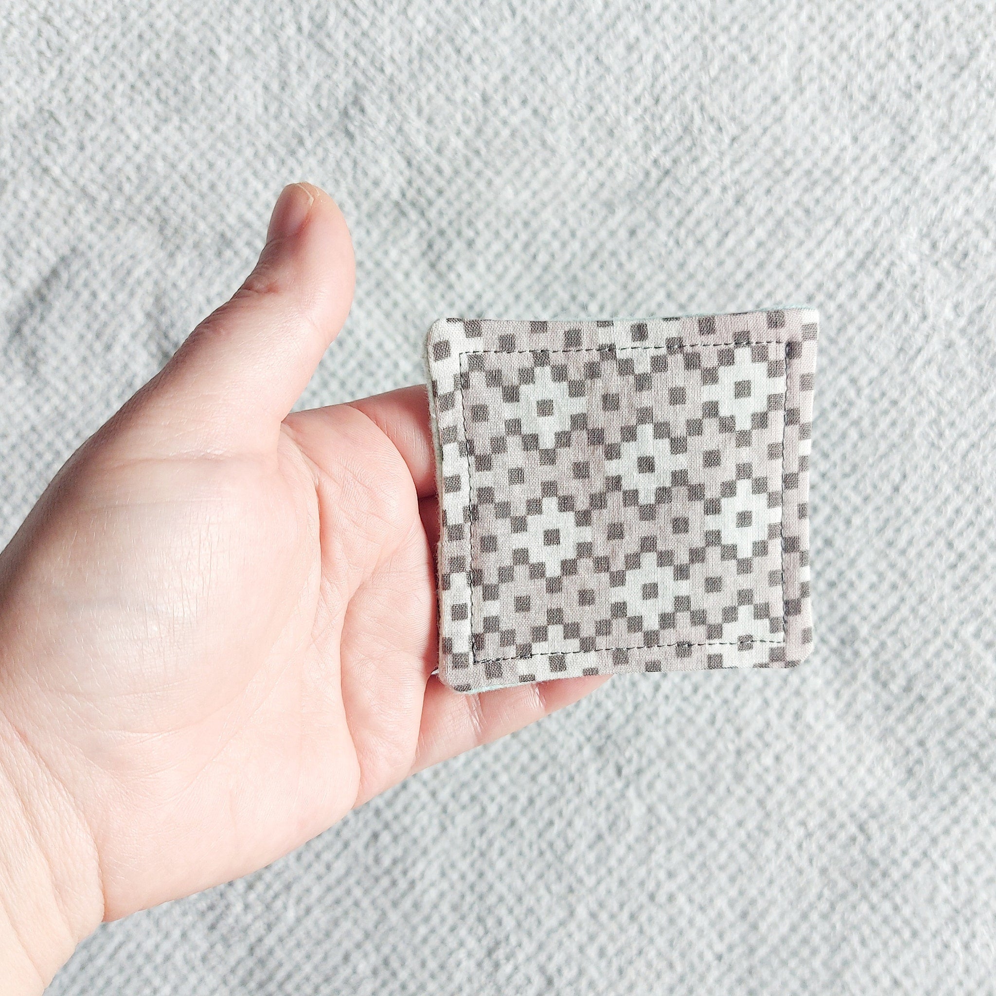 Square patterned fabric pad, gray and white geometric pattern, held in hand