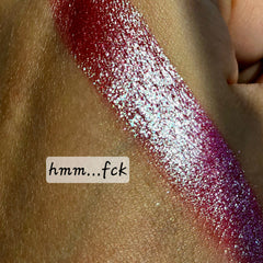 Close-up of fingertips applying shimmery multichrome eyeshadow with color-shifting purple to green hues