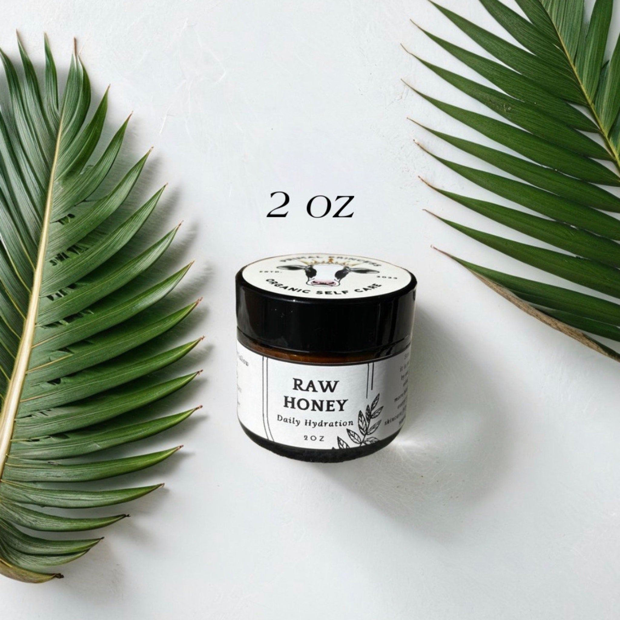 Raw honey jar with black lid, white label, and green leaves on white background