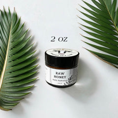 Raw honey jar with black lid, white label, and green leaves on white background