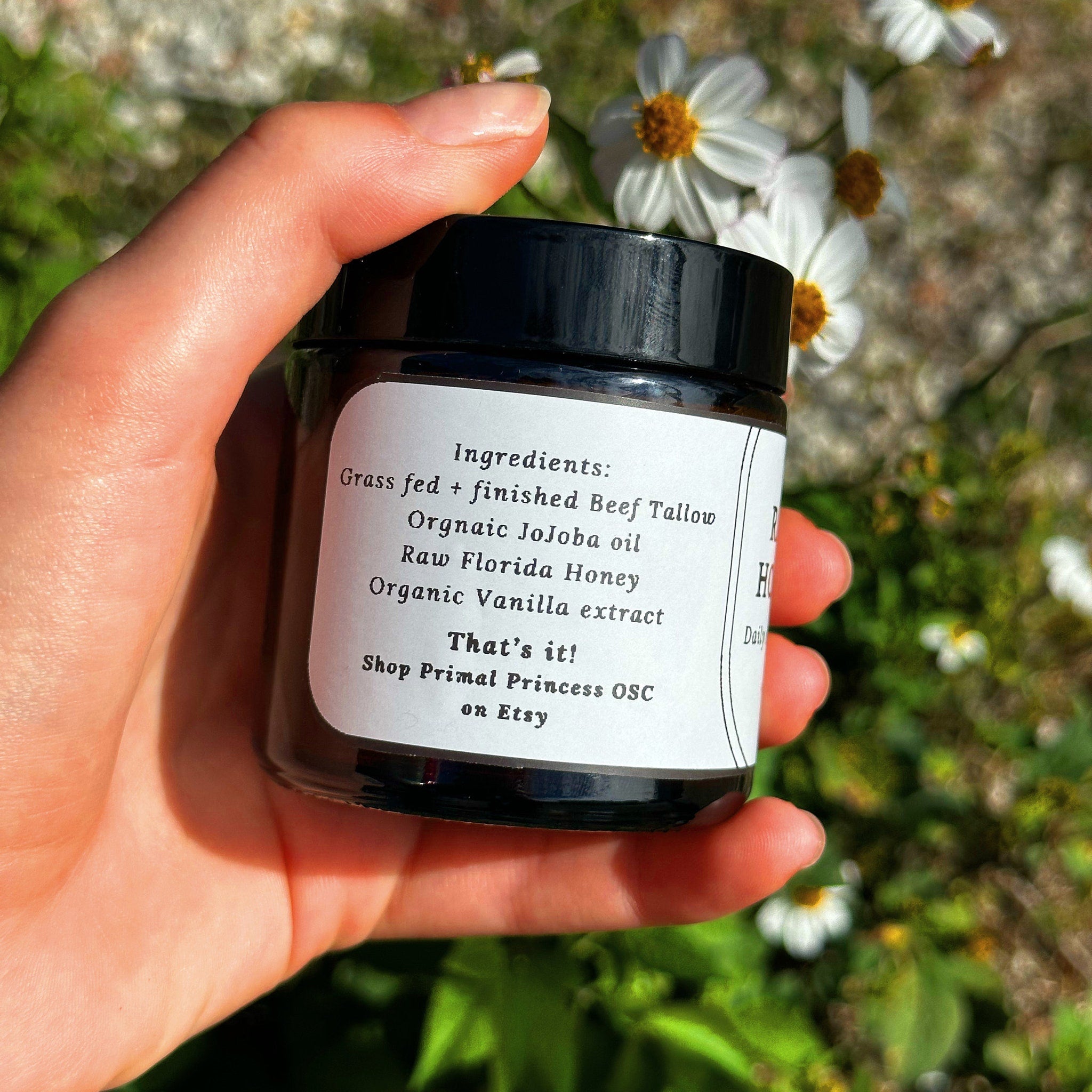 Jar of black glass with white label, held in hand near flowers, Primal Princess OSC text