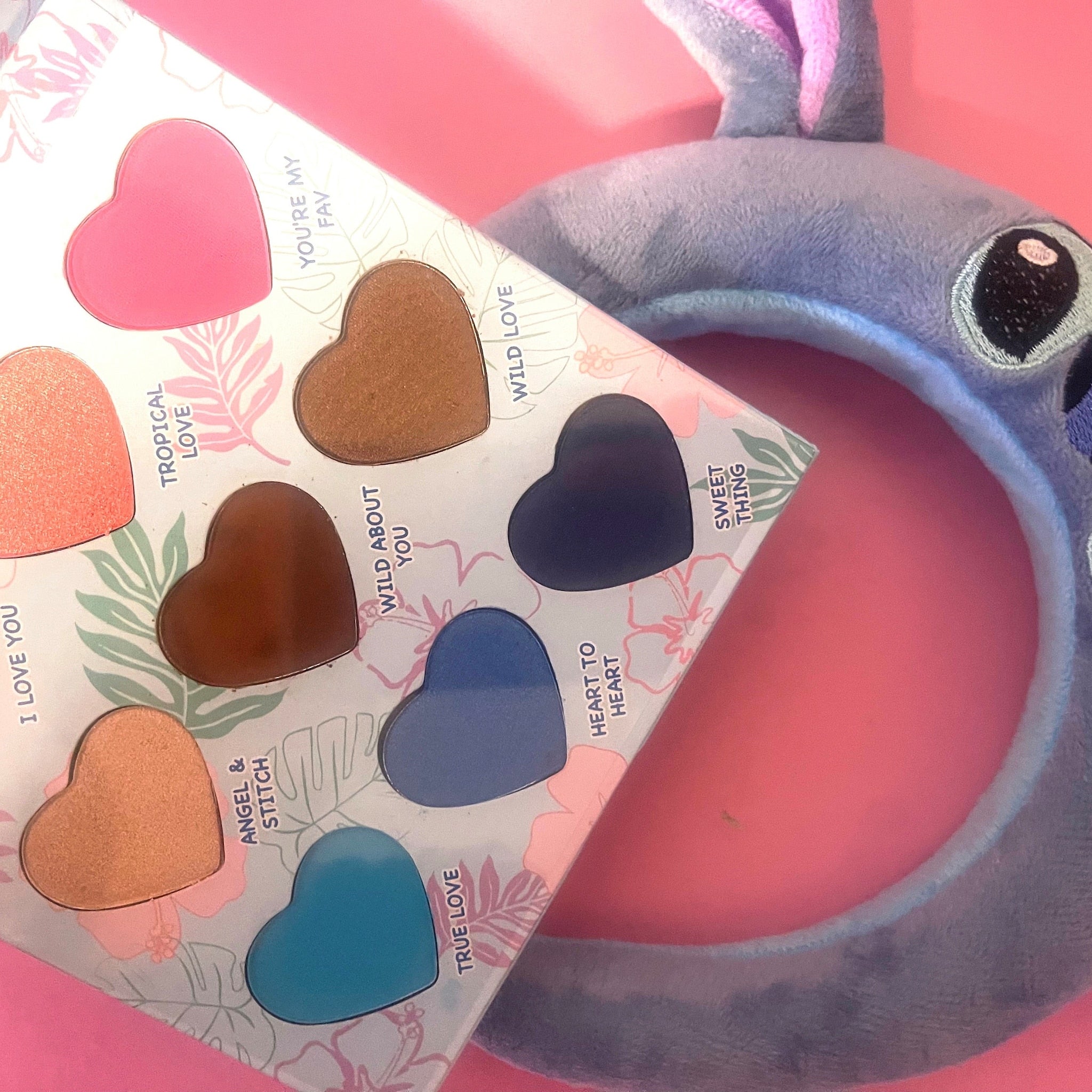 Heart-shaped eyeshadow palette with various colors and floral design, next to a blue plush headband