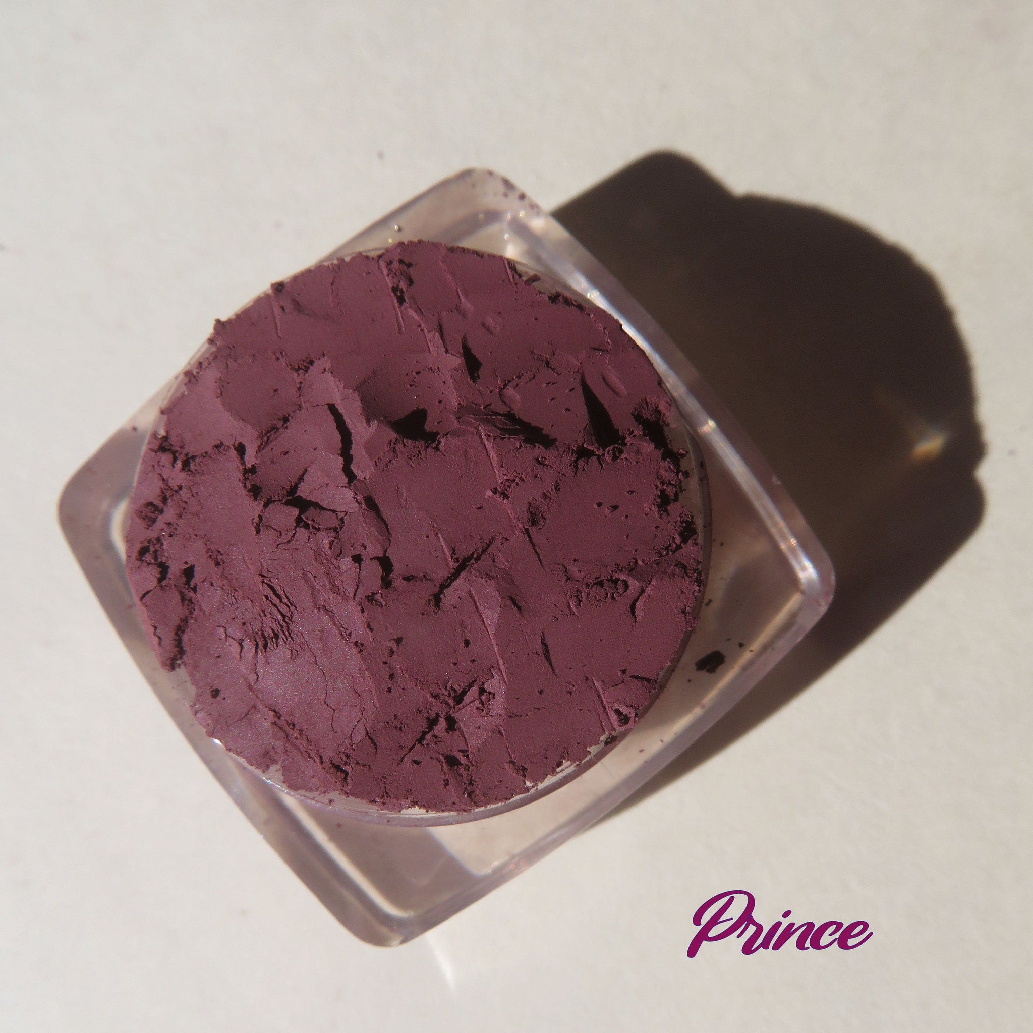 Close-up of dark mauve matte loose pigment with purple shimmer particles in compact case