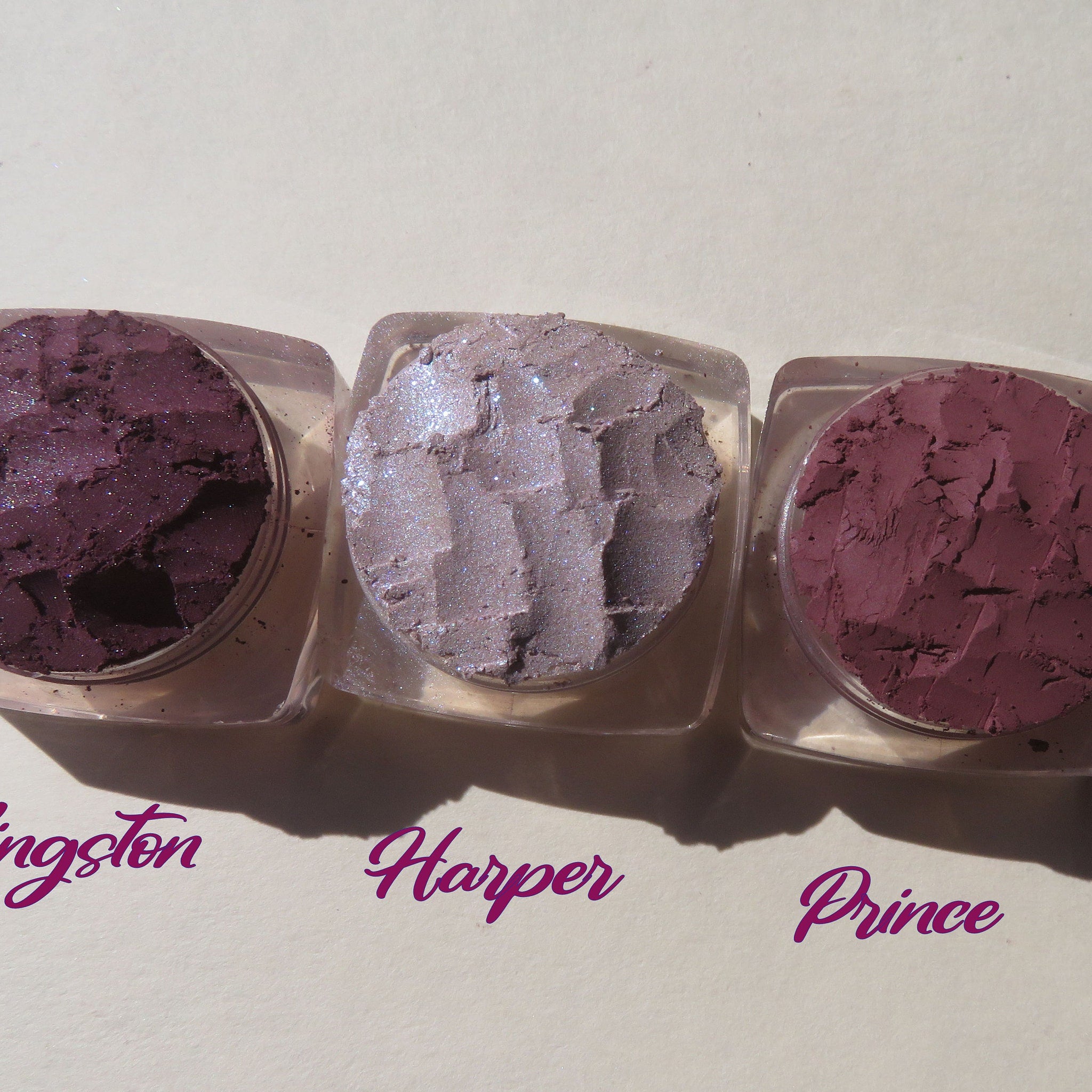 Three vegan loose pigment eyeshadows in dark mauve matte and purple shimmer shades displayed in round jars