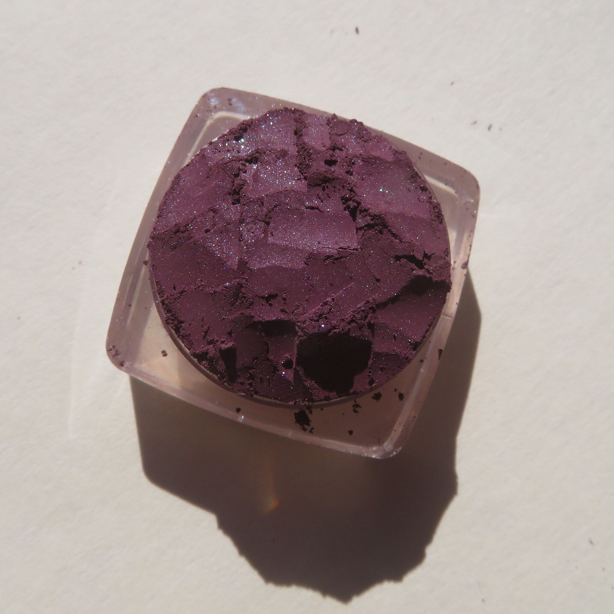Close-up of loose dark purple shimmer eye shadow with mineral sparkle, showcasing fine vegan powder texture