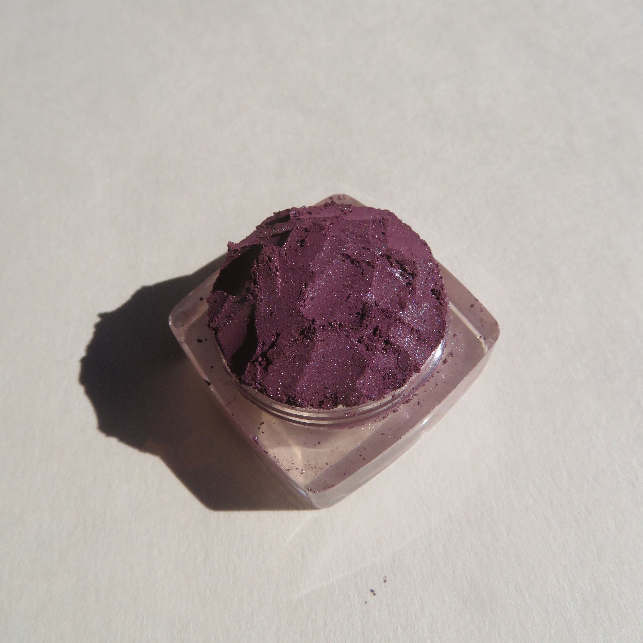 Side view of dark purple shimmer loose mineral eye shadow in eco-friendly packaging, showcasing rich pigment texture