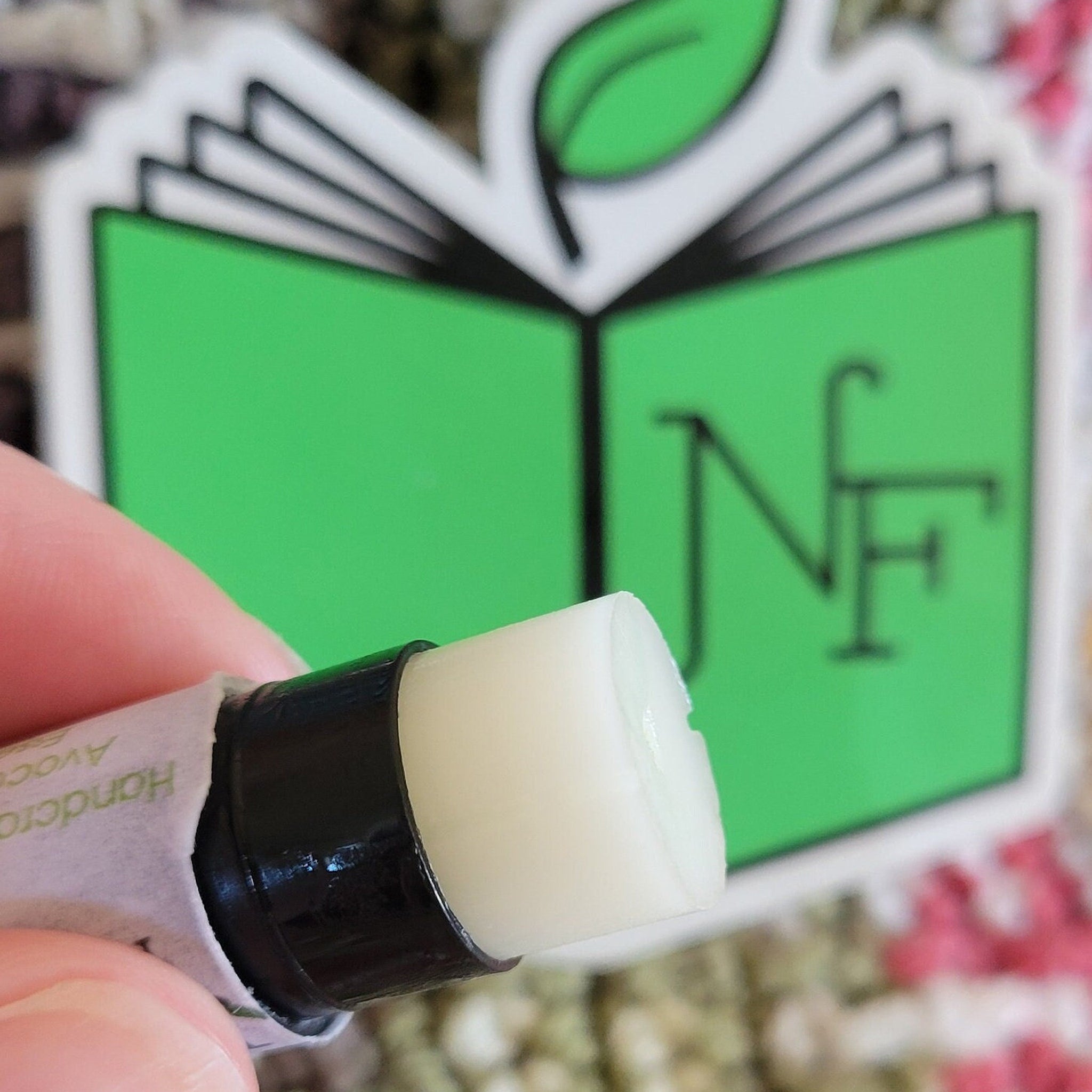 Lip balm stick with white balm, black tube, and "Handcrafted" label visible