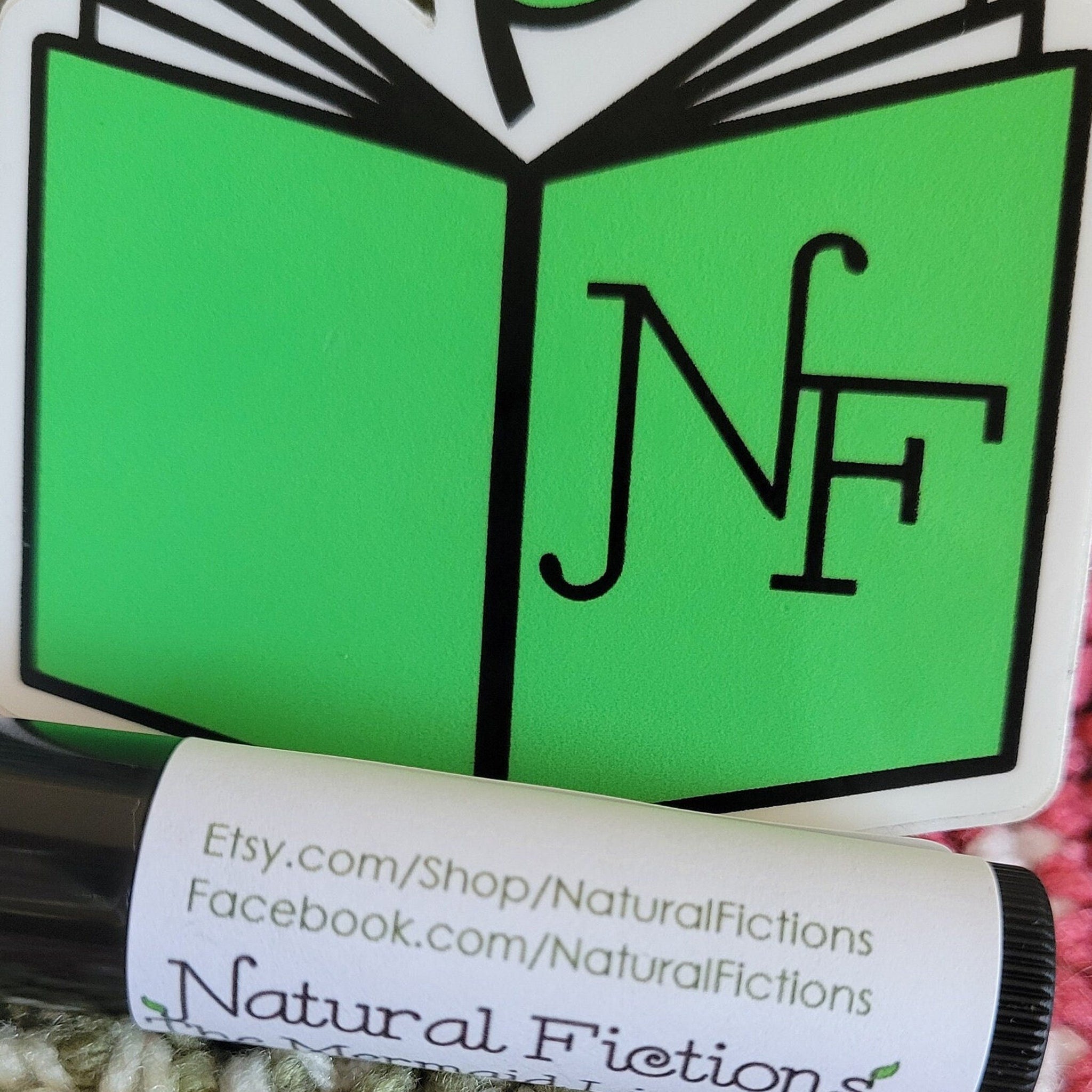 Natural Fiction lip balm with black tube and white label, green logo sticker in background