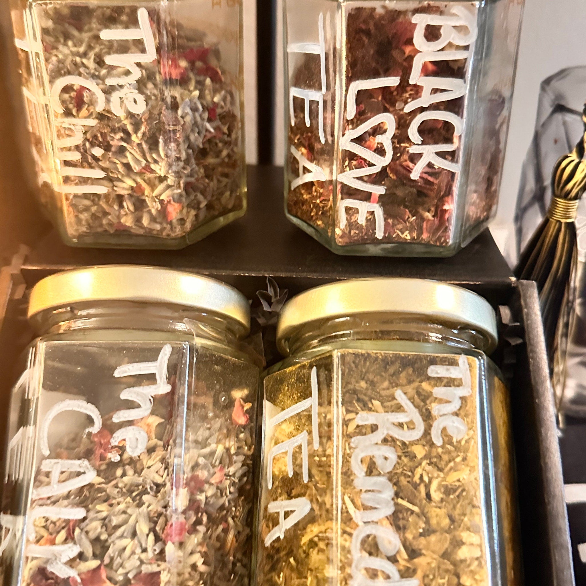 Tea jars with white text labels, glass jars filled with dried herbs and flowers, gold lids