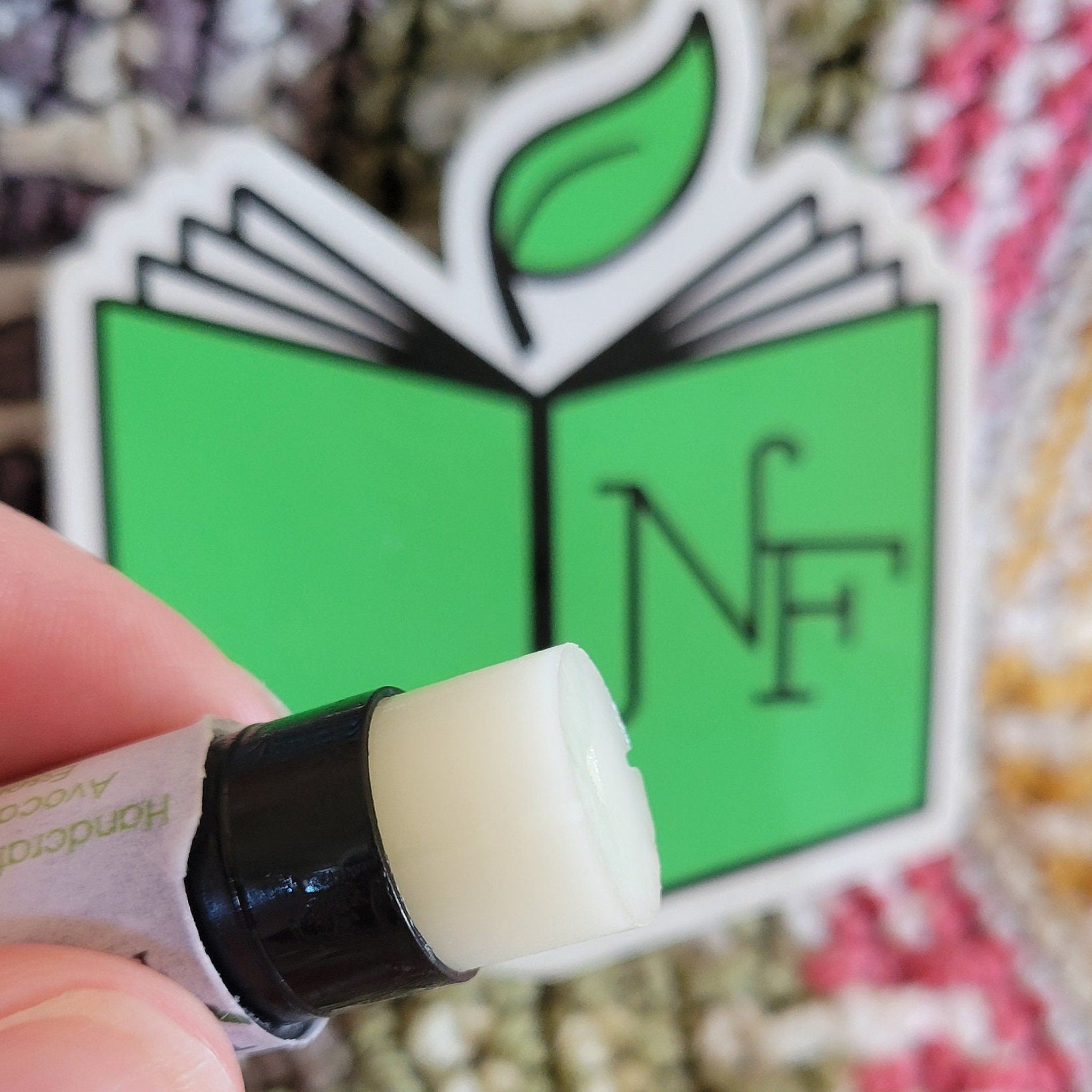 Lip balm with white and black tube, held by hand, with green and white label visible