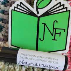 Lip balm tube with black and white label, green logo, and Natural Fictions text on a textured background