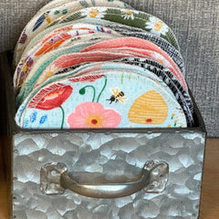 Cotton rounds with floral patterns and white stitching, stacked in metal container