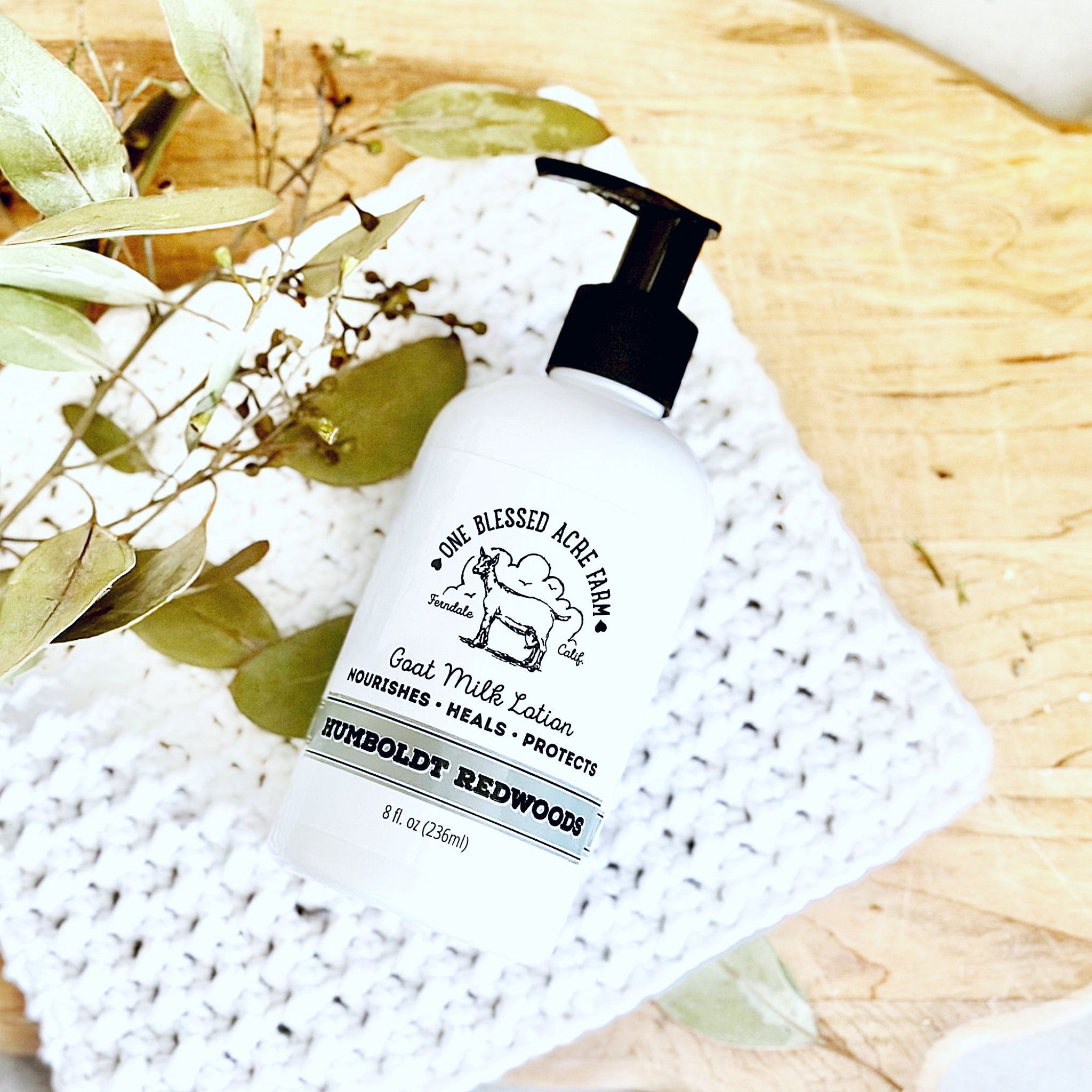 Goat milk lotion bottle with black pump, white label, and white crochet blanket on wood surface