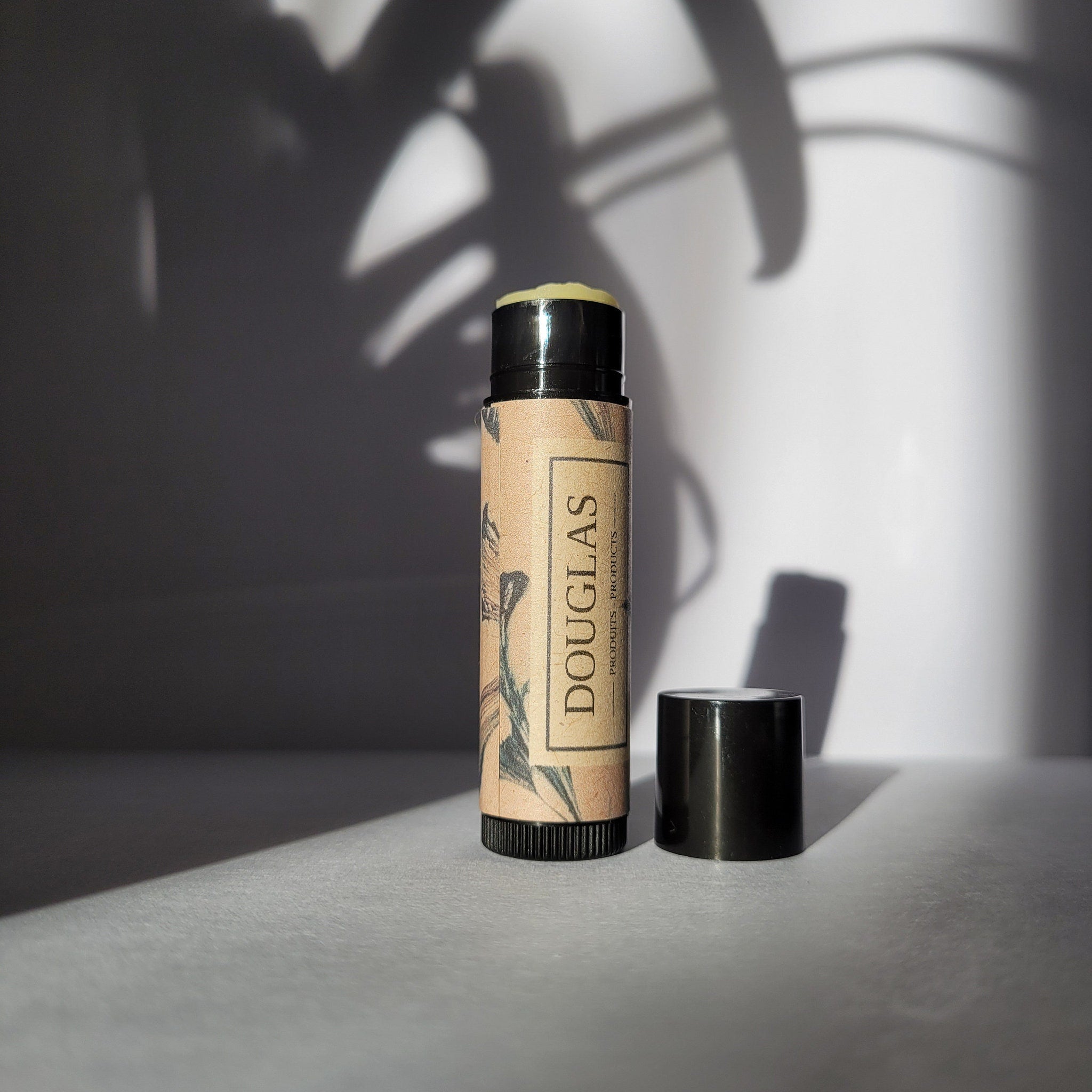 Lip balm tube with brown paper label, black cap, and "DOUGLAS" text visible