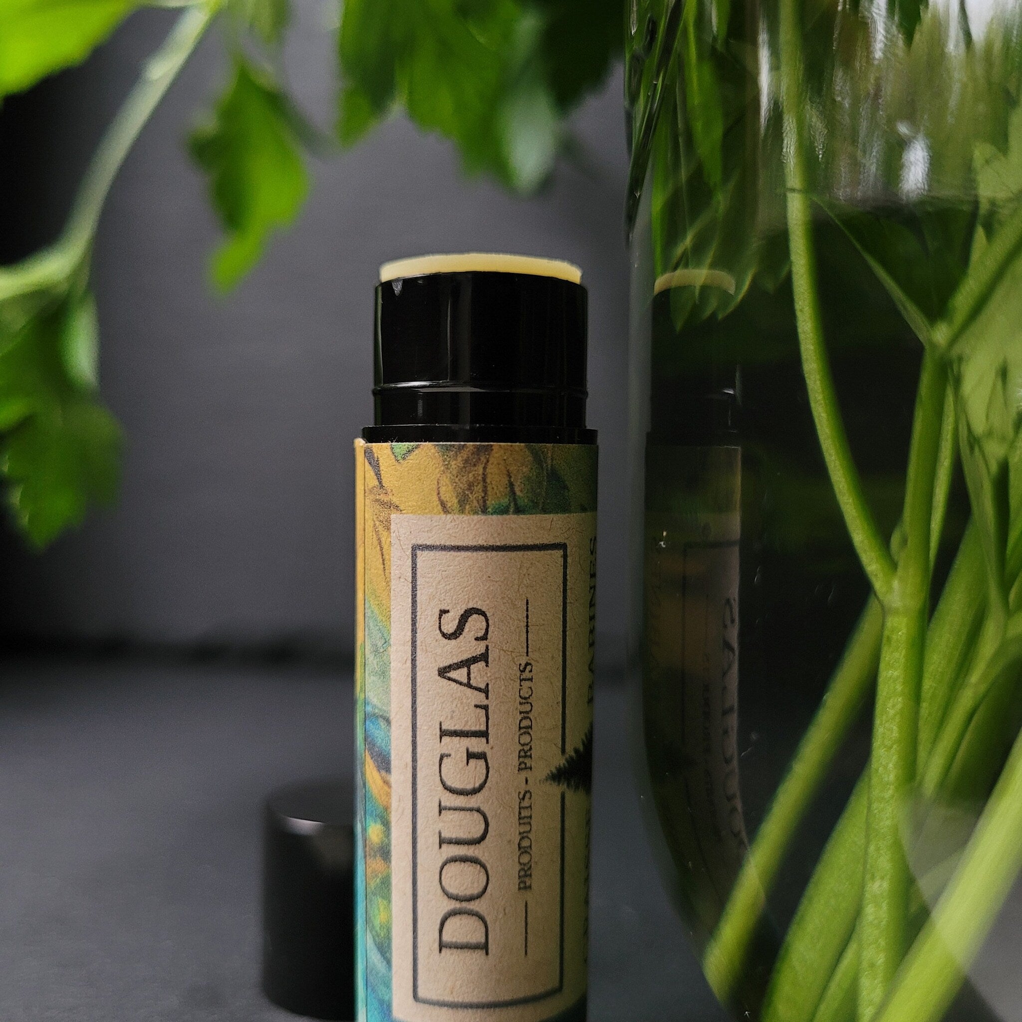Lip balm tube with black cap, yellow and patterned label, and "DOUGLAS" text visible