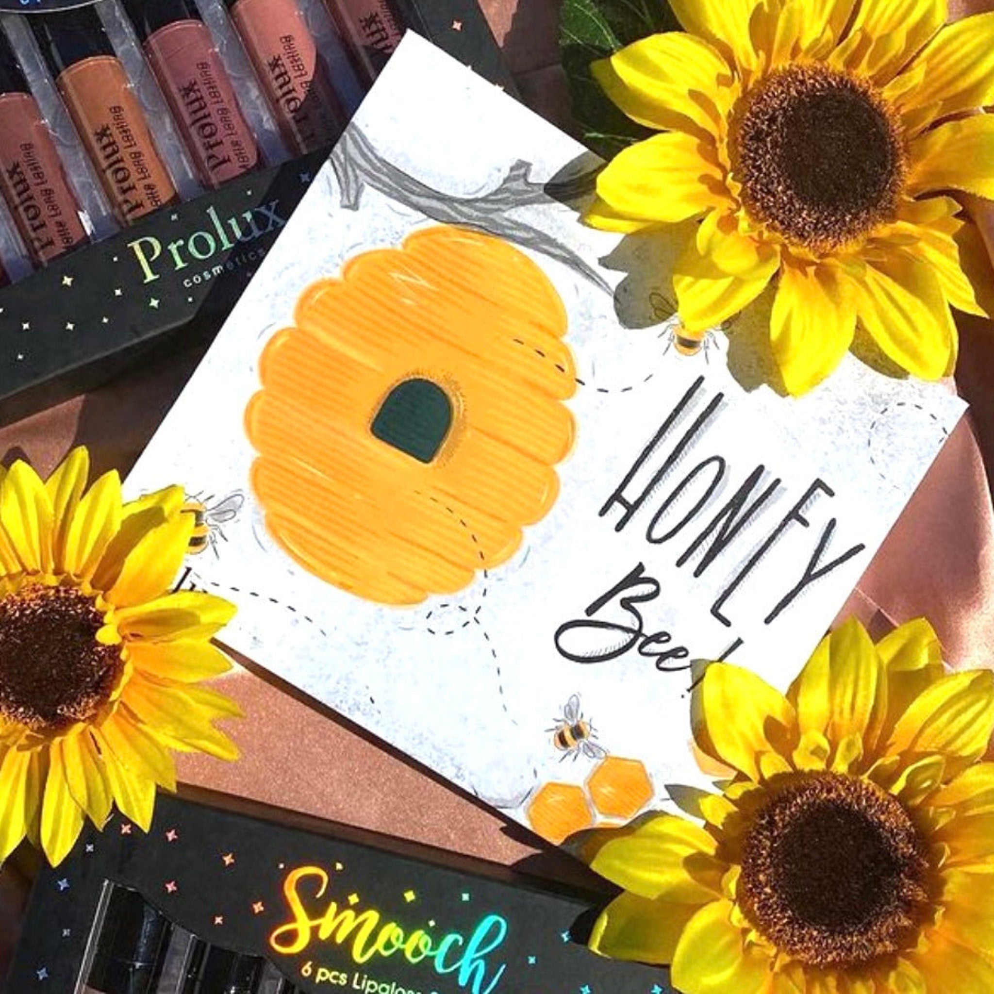 Lip gloss set with Prolux brand, yellow sunflowers, and honey bee drawing on white paper