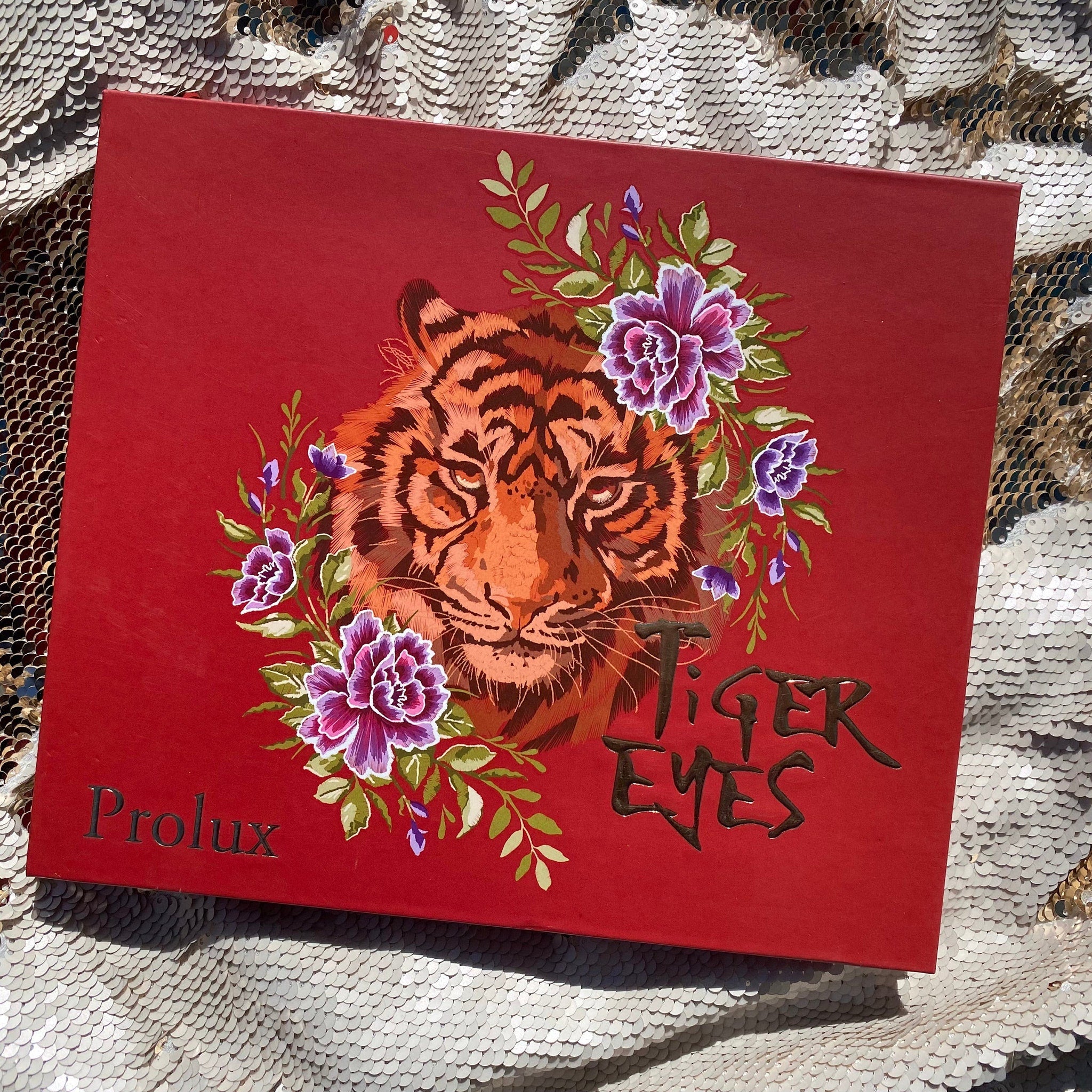 Red box with tiger illustration, floral accents, and "Tiger Eyes" text on a sequin surface